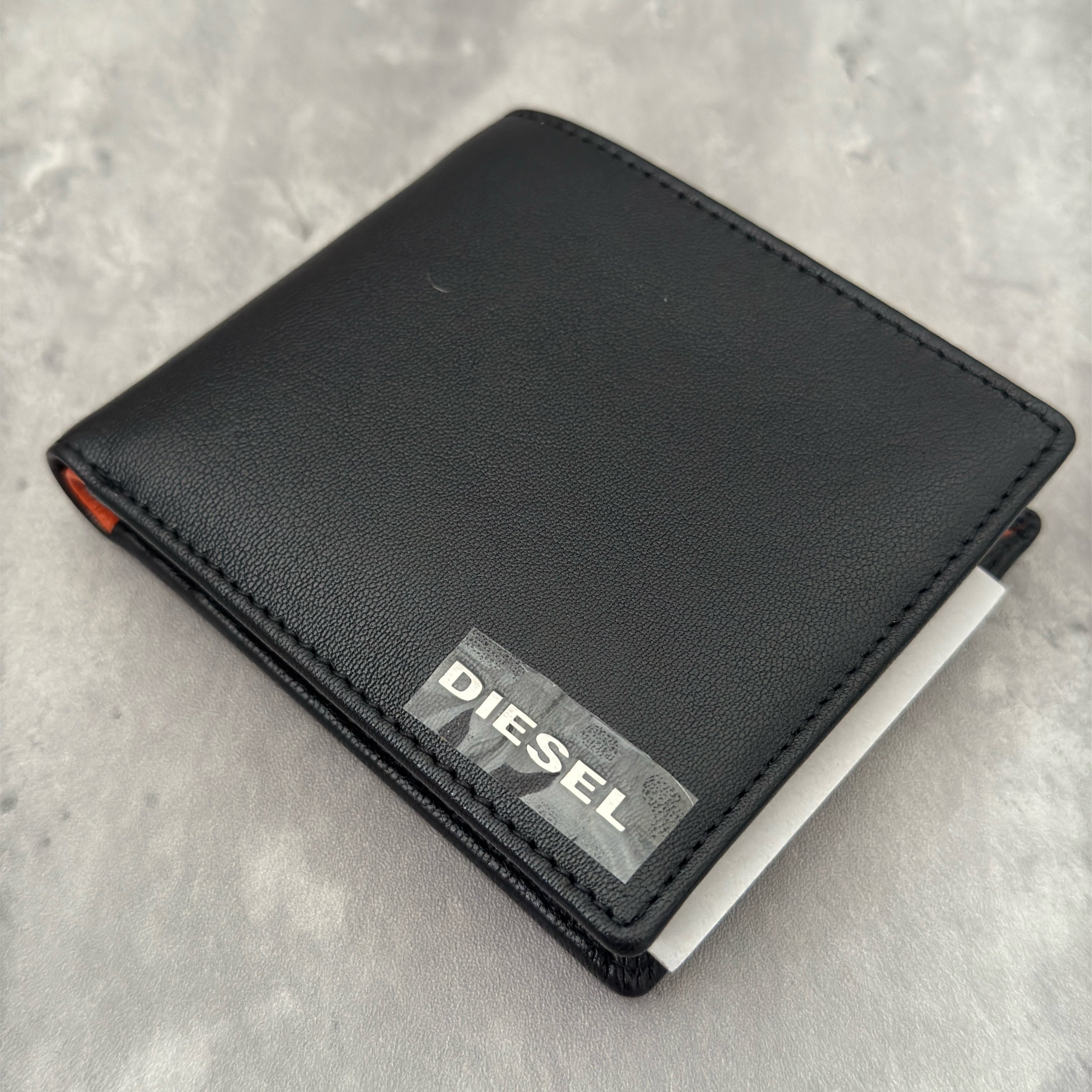 Diesel Signature Leather Wallet in black with contrast orange interior, featuring a metal logo plaque and multiple compartments.