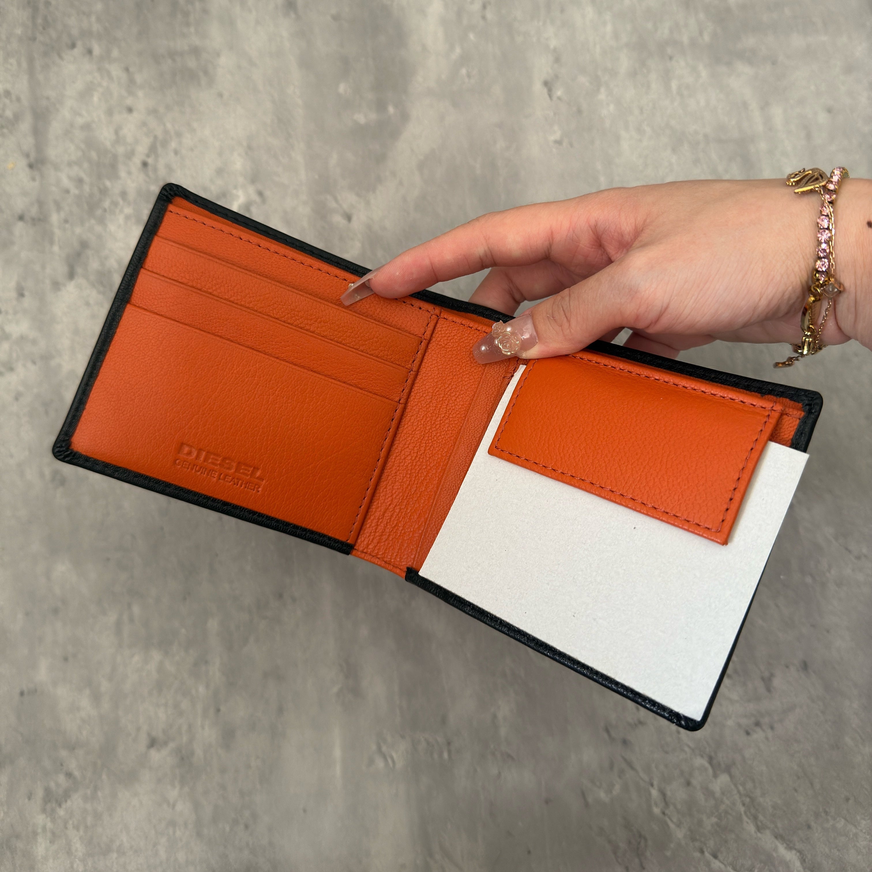 Diesel Signature Leather Wallet in black with contrast orange interior, featuring a metal logo plaque and multiple compartments.