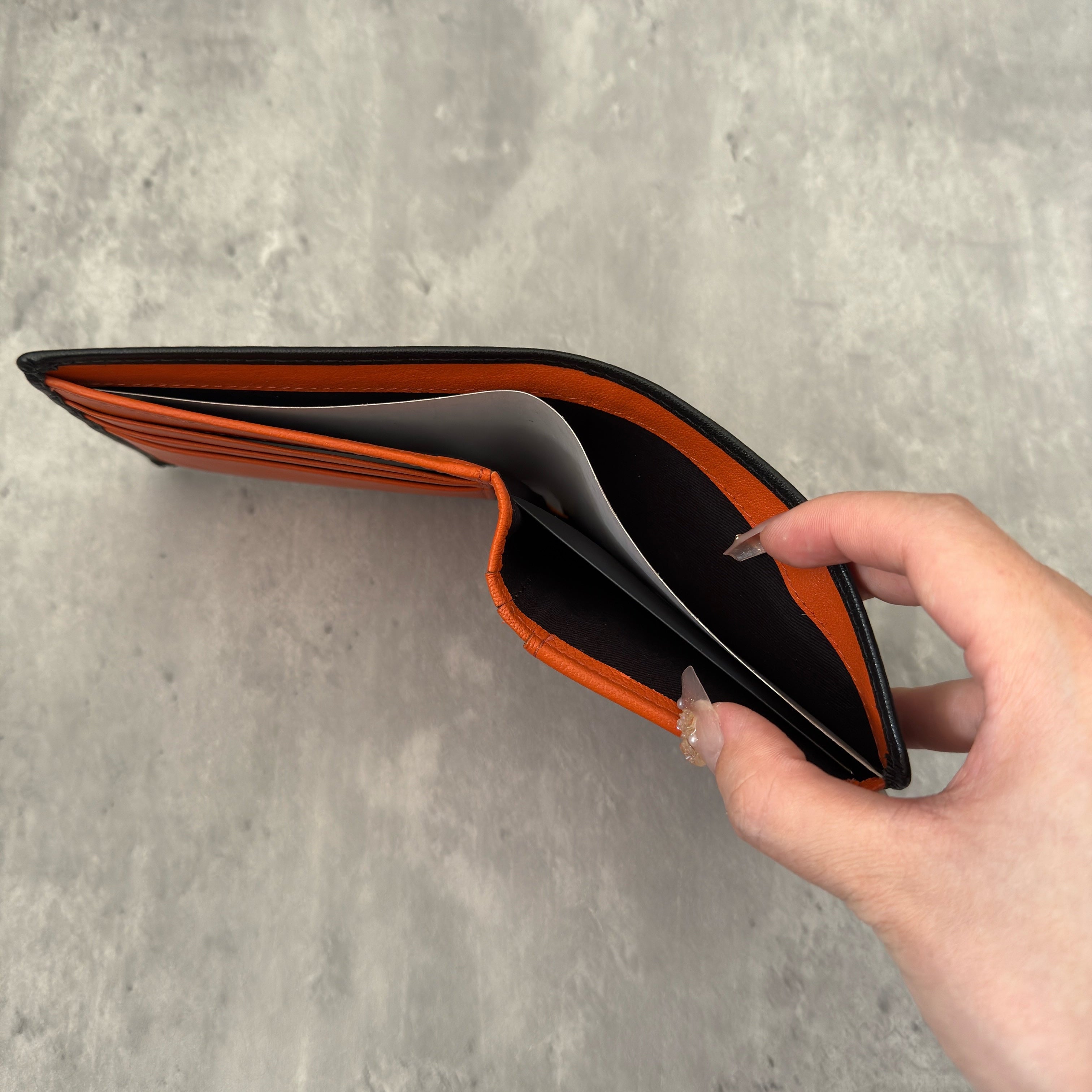 Diesel Signature Leather Wallet in black with contrast orange interior, featuring a metal logo plaque and multiple compartments.