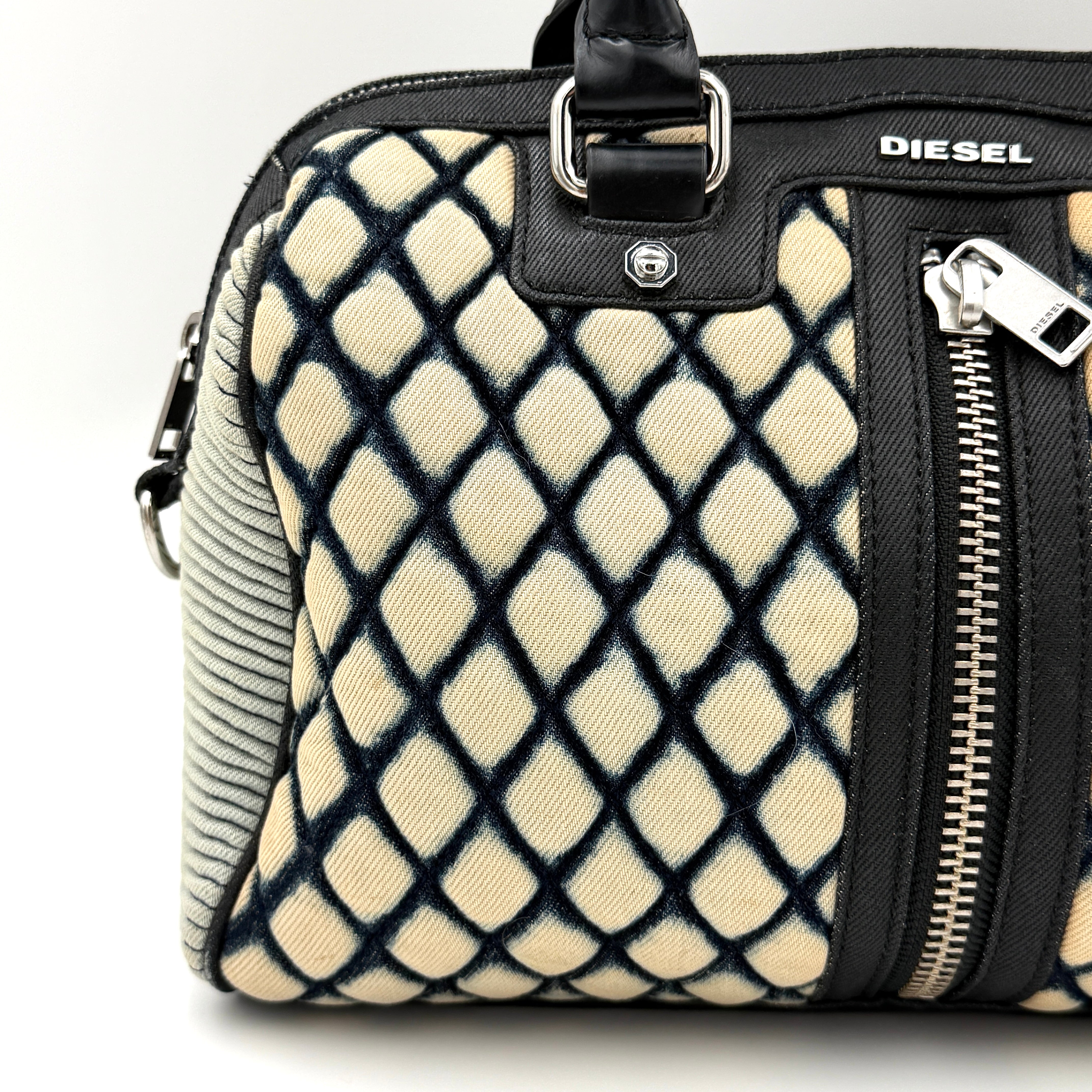 Diesel 2Way Boston Handbag in cream canvas with black velvet-effect lattice, dual leather handles, and detachable strap displayed in front.