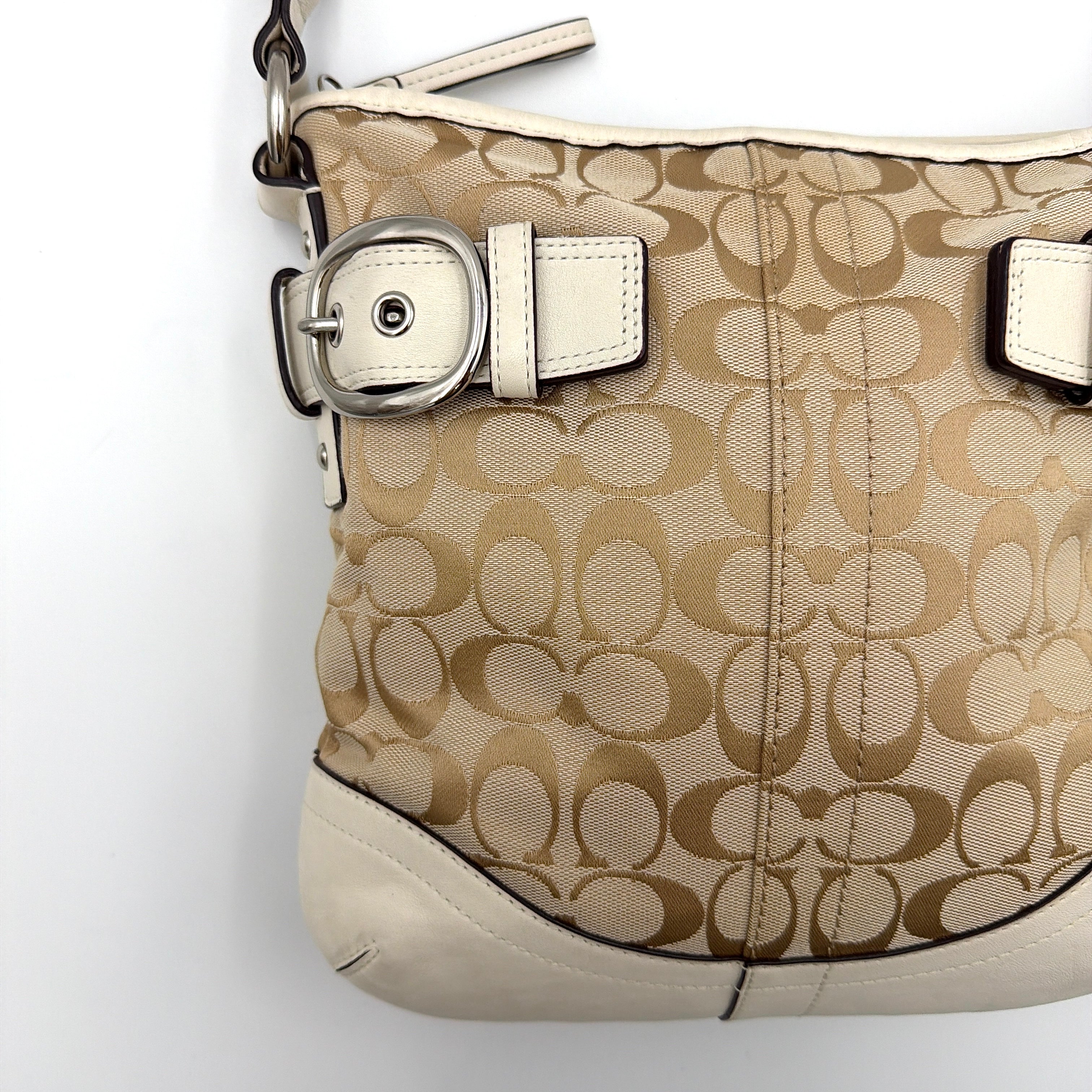 Coach beige and white signature canvas shoulder bag with white leather trim, silver buckles, and adjustable strap on display.