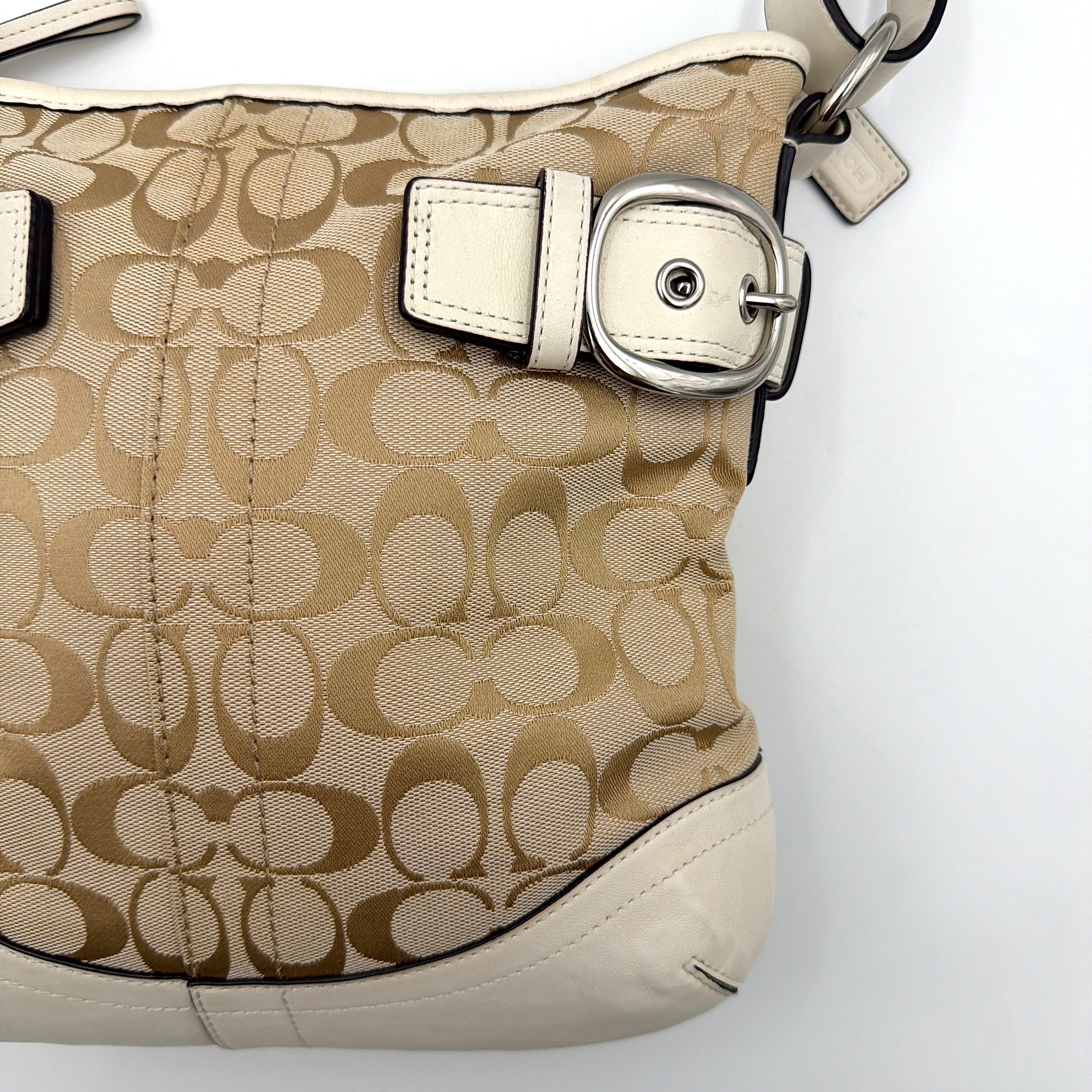 Coach beige and white signature canvas shoulder bag with white leather trim, silver buckles, and adjustable strap on display.