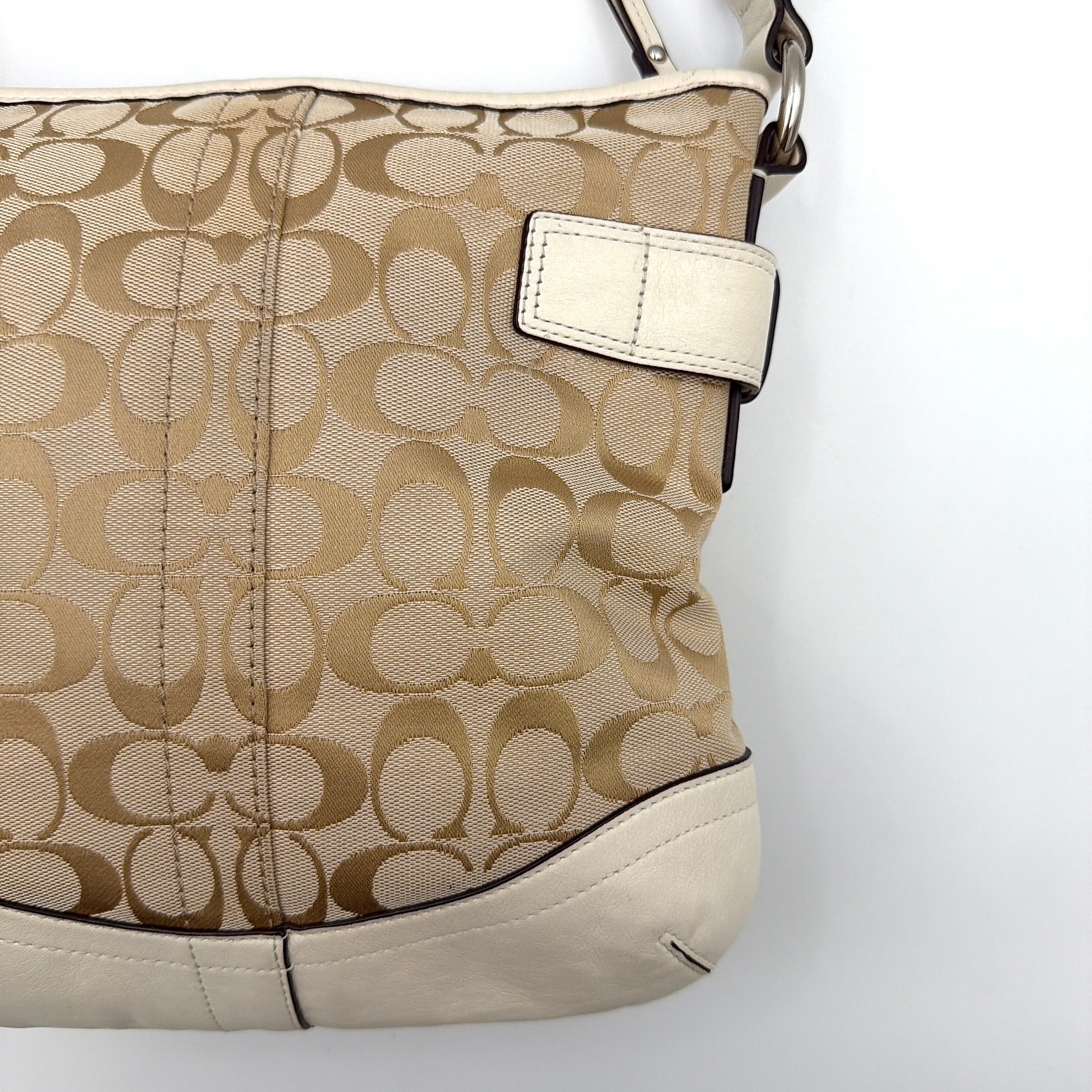 Coach beige and white signature canvas shoulder bag with white leather trim, silver buckles, and adjustable strap on display.