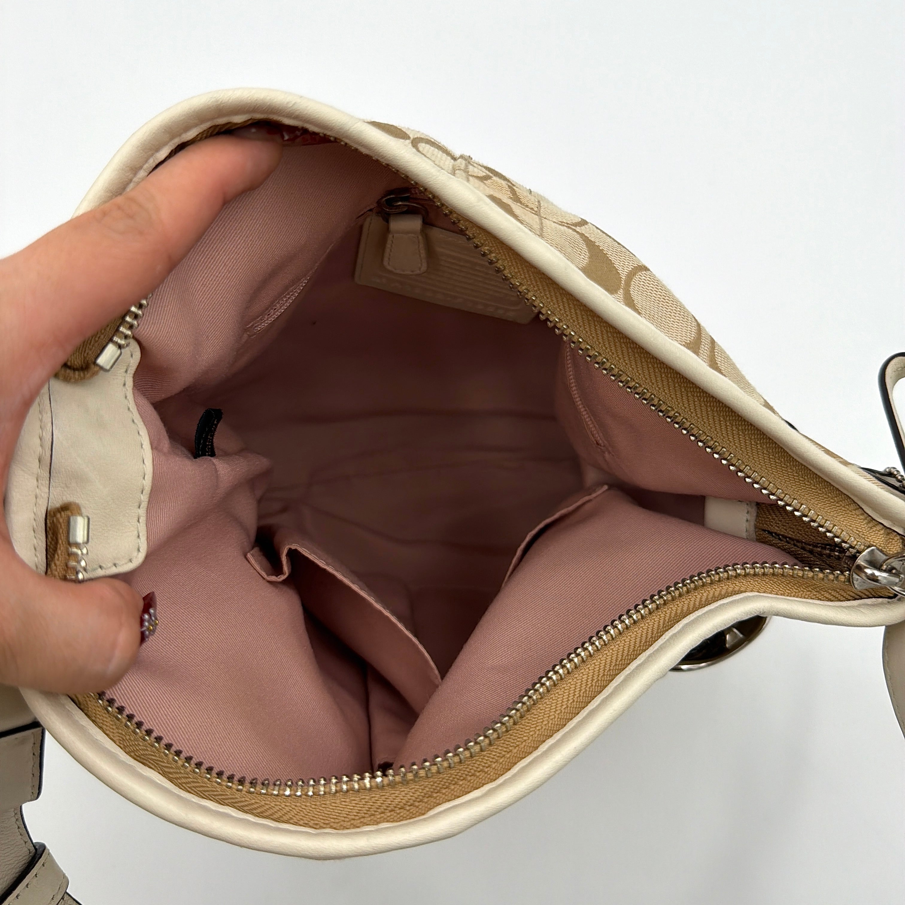 Coach beige and white signature canvas shoulder bag with white leather trim, silver buckles, and adjustable strap on display.