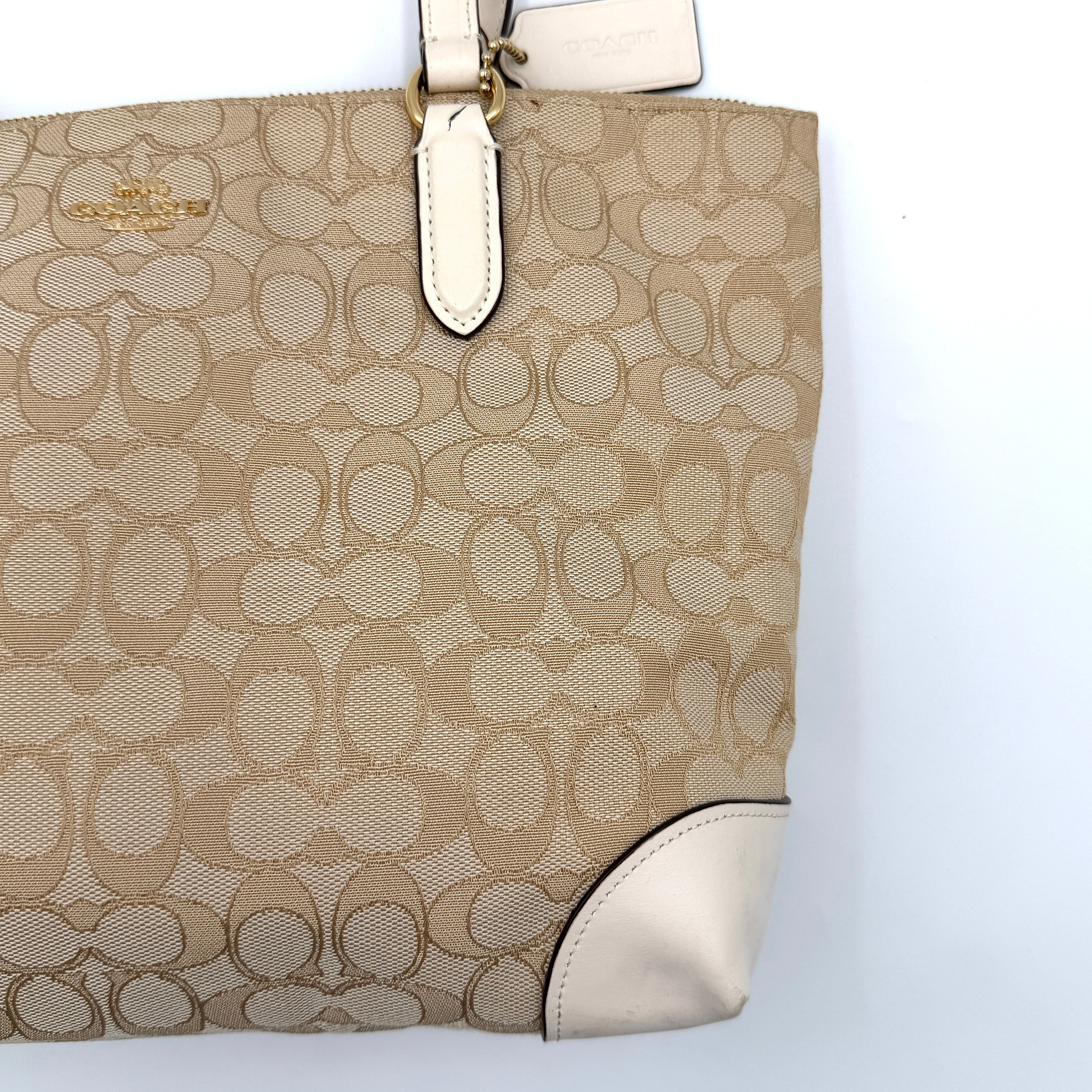 Coach Signature Zip Top Tote Bag in beige canvas with white leather trim and double handles, featuring the signature monogram print.