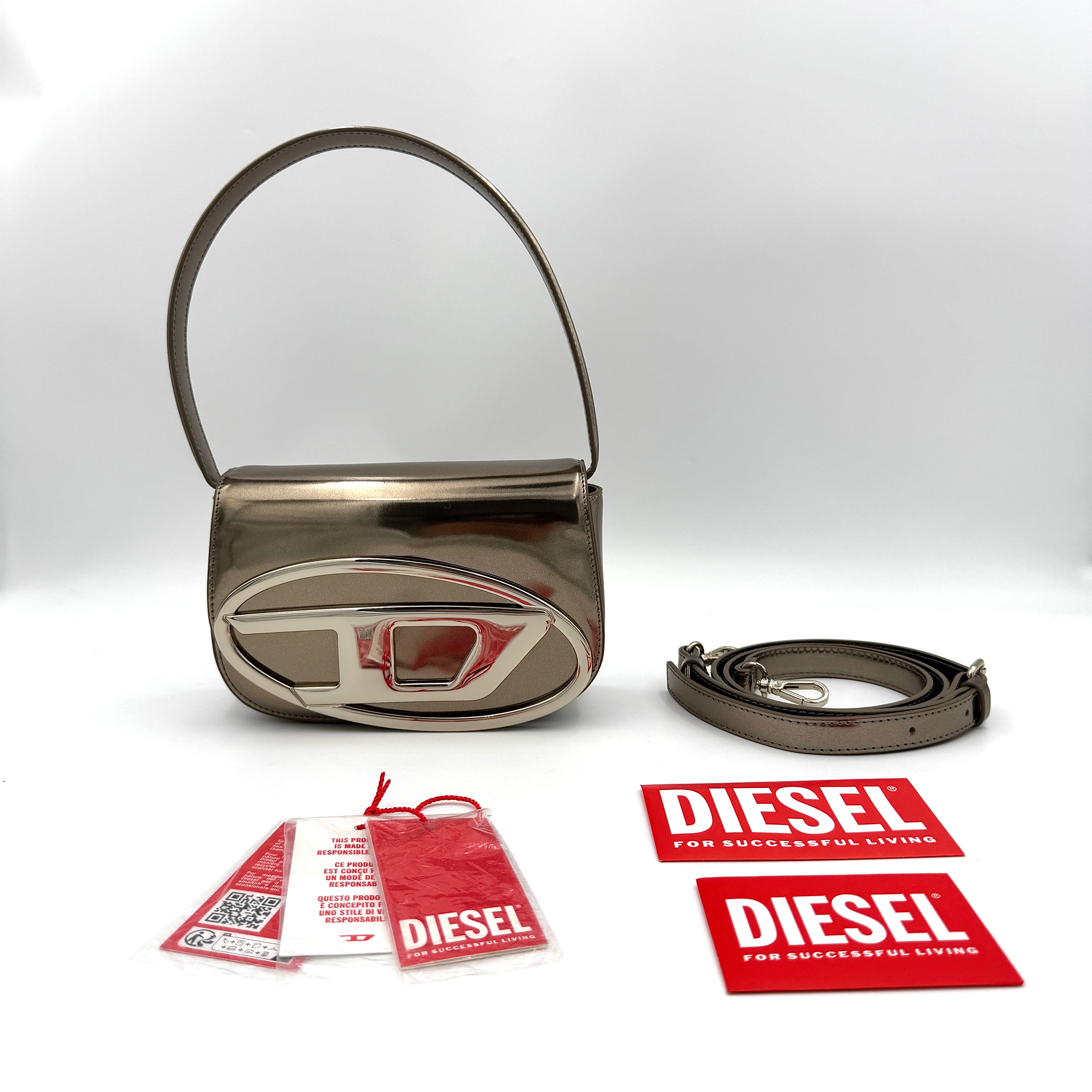 Diesel 1DR metallic silver shoulder bag with oversized chrome D-logo plaque, top handle, and detachable strap displayed against a white background.