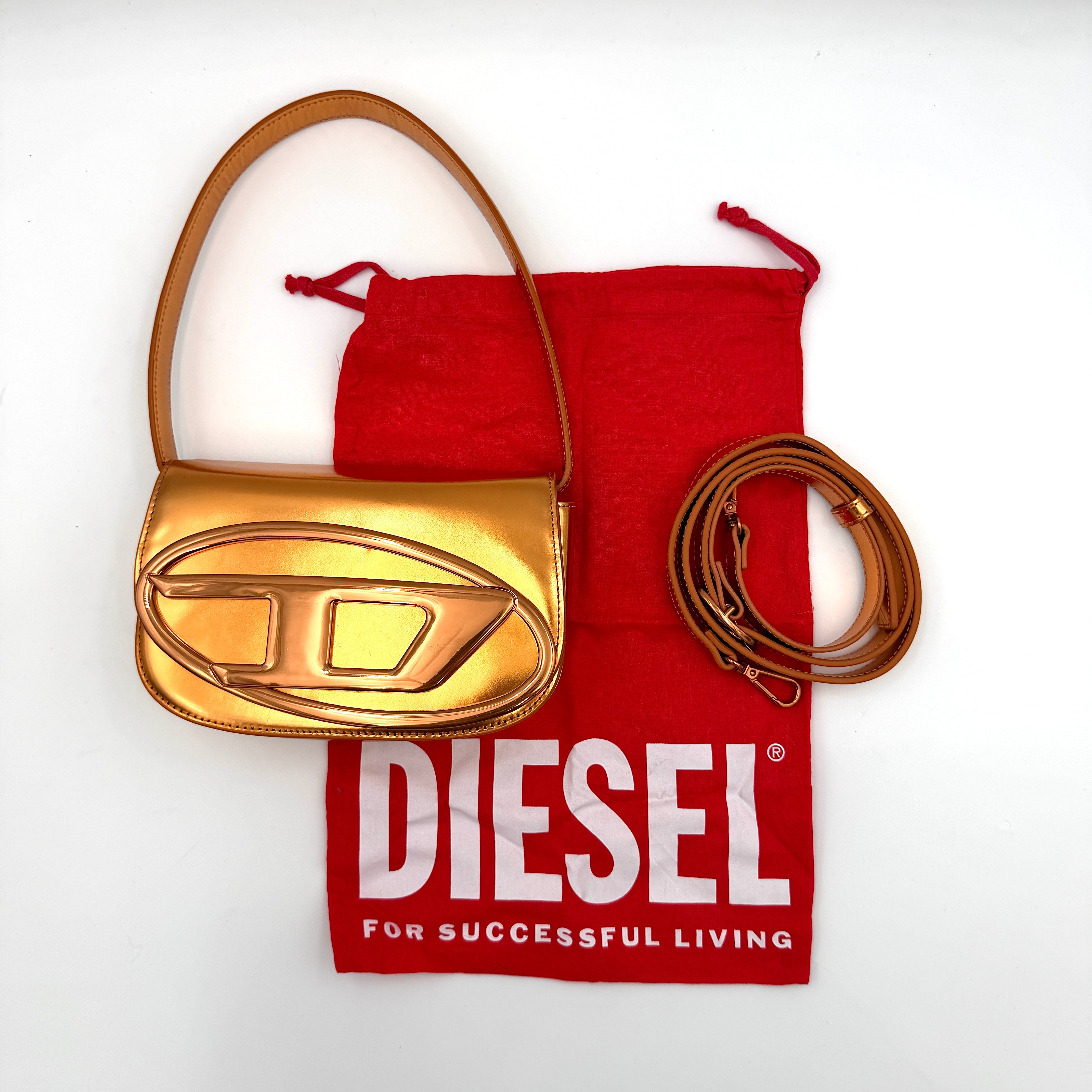 A Diesel 2Way 1DR Shoulder Bag in striking metallic gold with an embossed logo and detachable strap, displayed alongside its accessories.