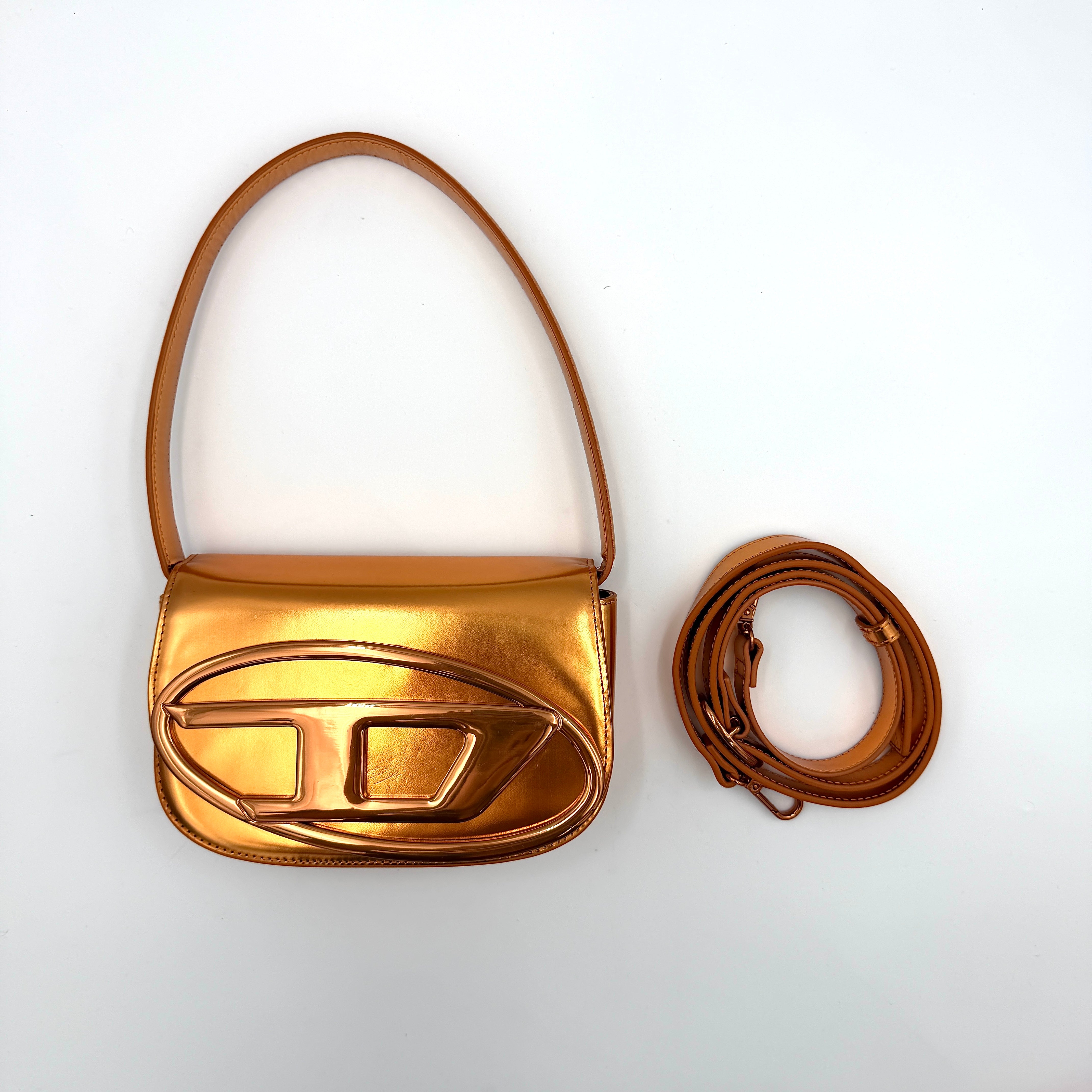 A Diesel 2Way 1DR Shoulder Bag in striking metallic gold with an embossed logo and detachable strap, displayed alongside its accessories.