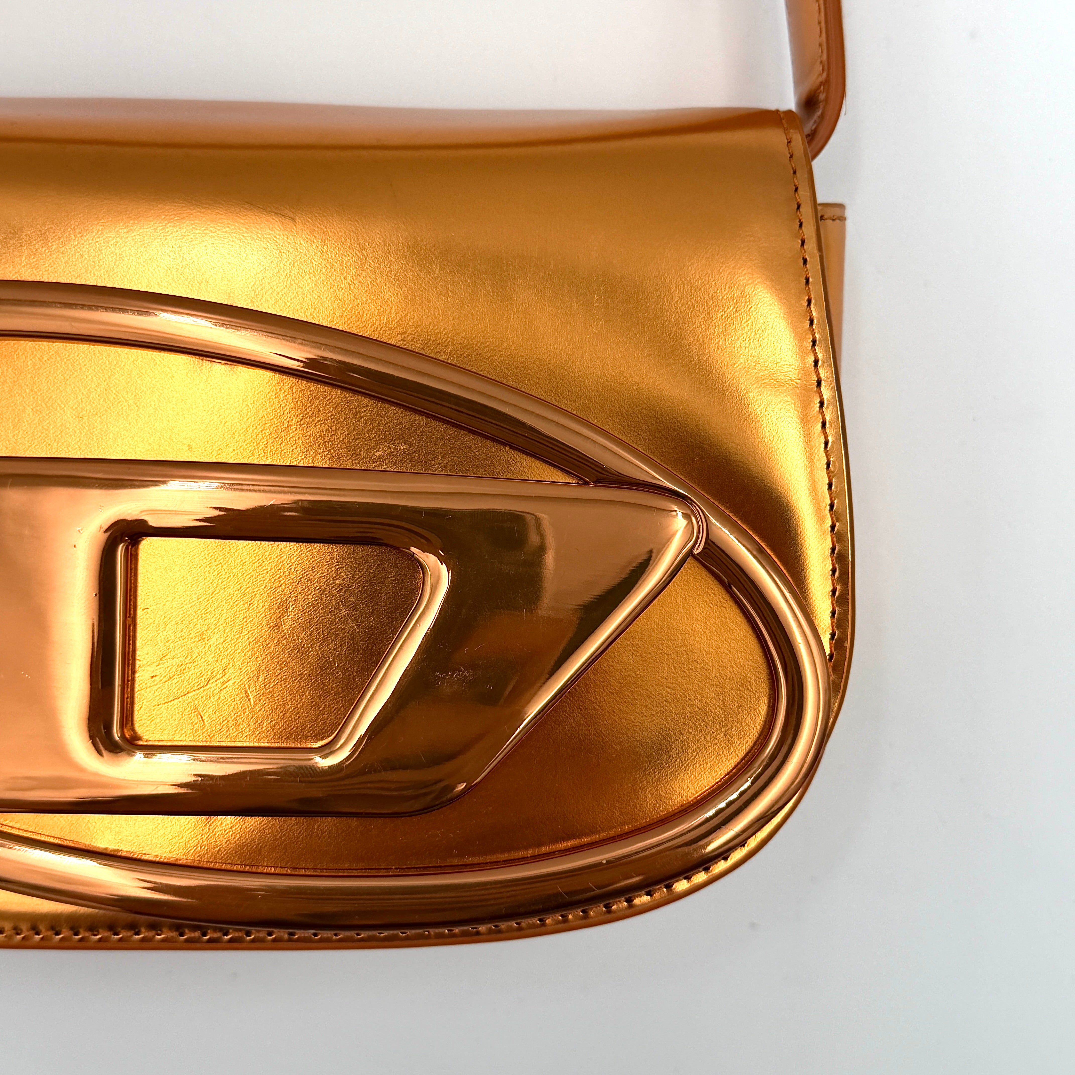A Diesel 2Way 1DR Shoulder Bag in striking metallic gold with an embossed logo and detachable strap, displayed alongside its accessories.