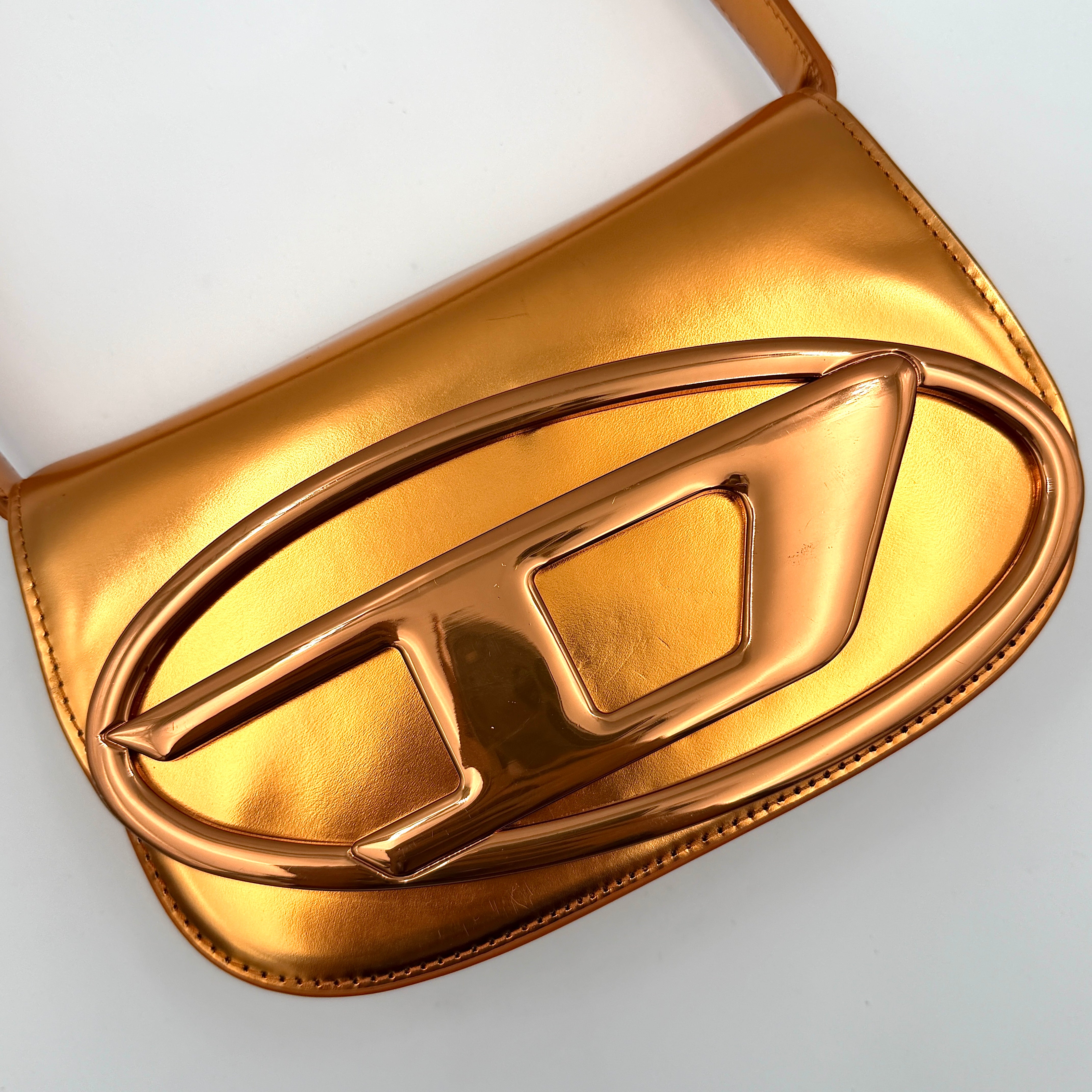 A Diesel 2Way 1DR Shoulder Bag in striking metallic gold with an embossed logo and detachable strap, displayed alongside its accessories.