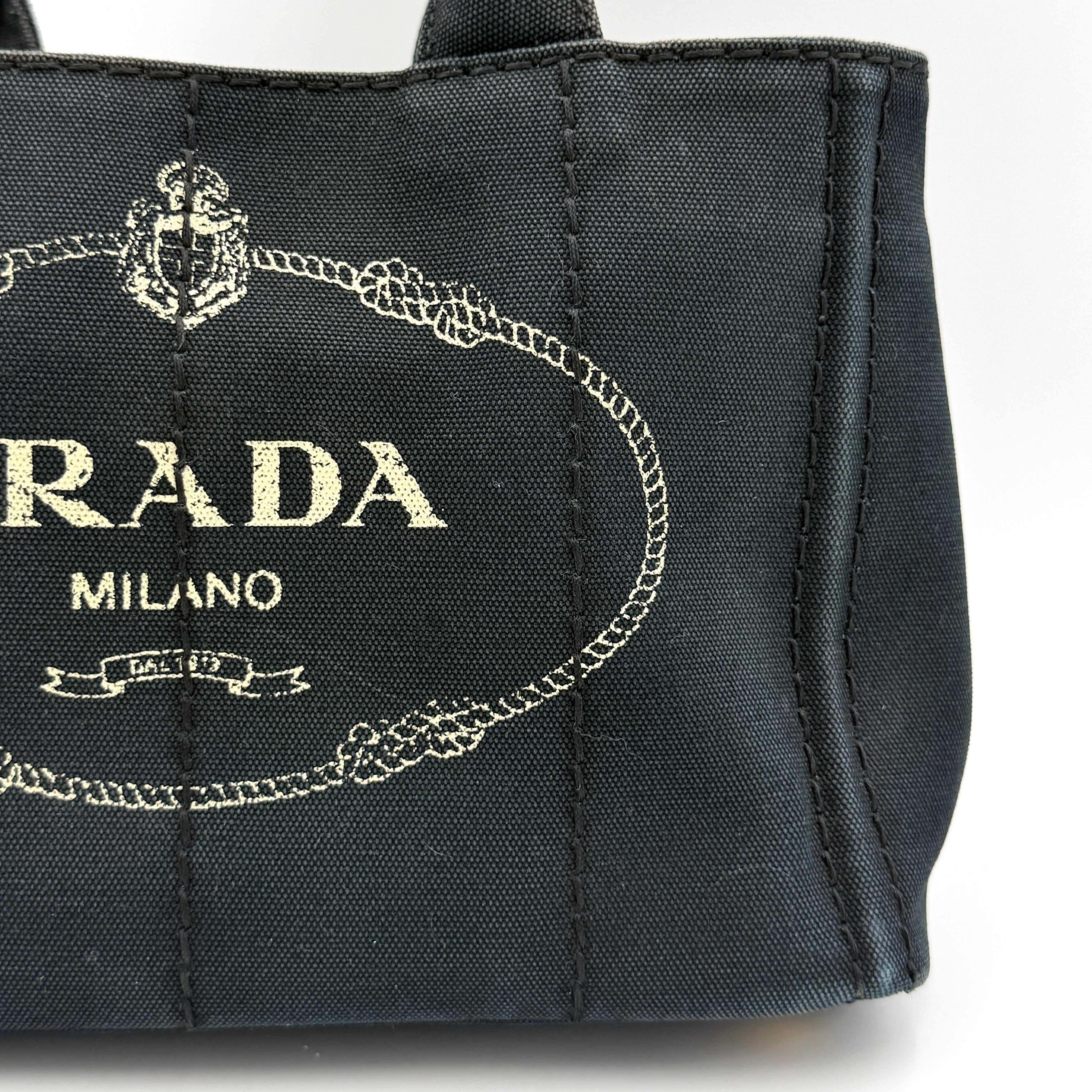 Front-facing Prada Canapa Embroidered Logo Tote in black canvas with ivory stitched logo and double handles.