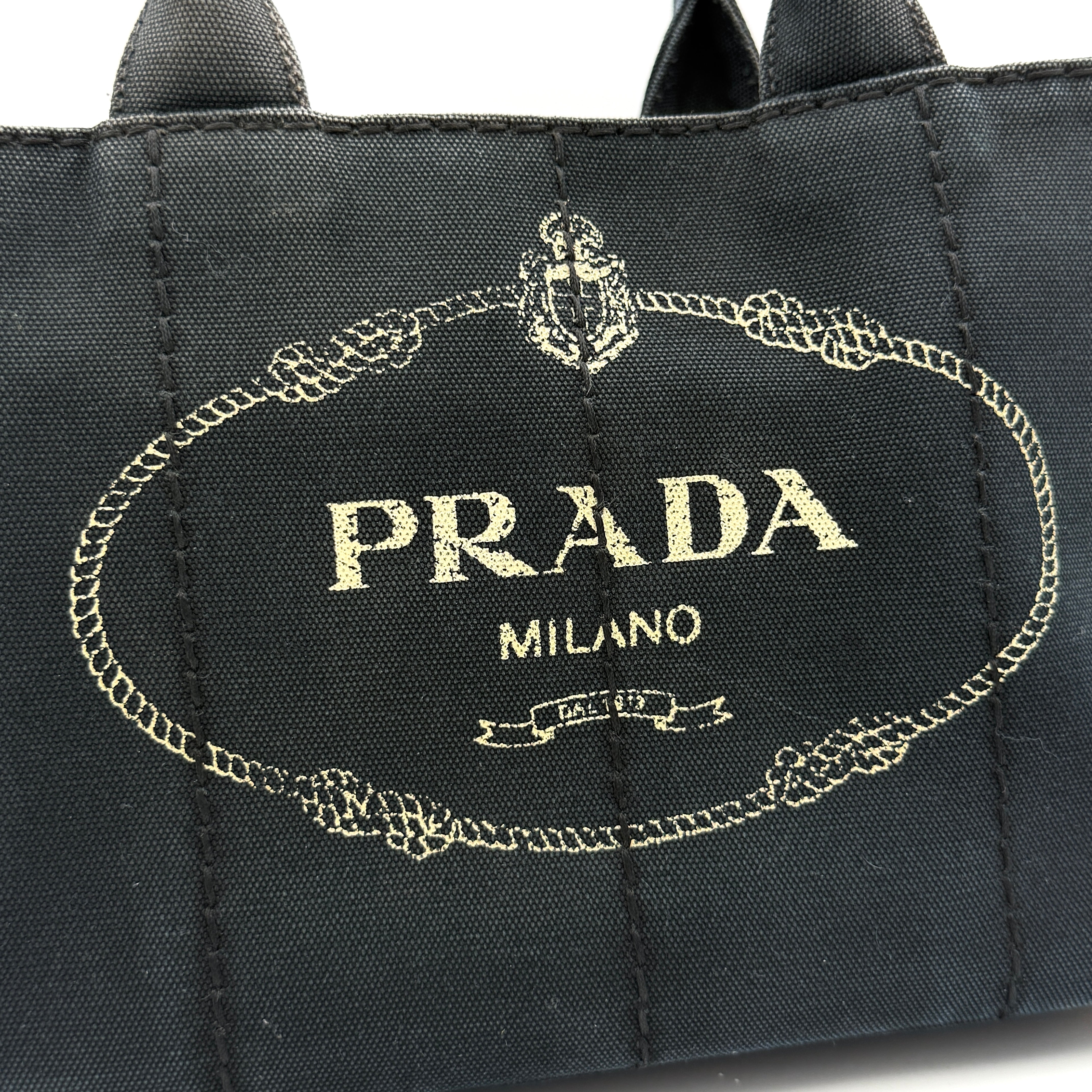Front-facing Prada Canapa Embroidered Logo Tote in black canvas with ivory stitched logo and double handles.