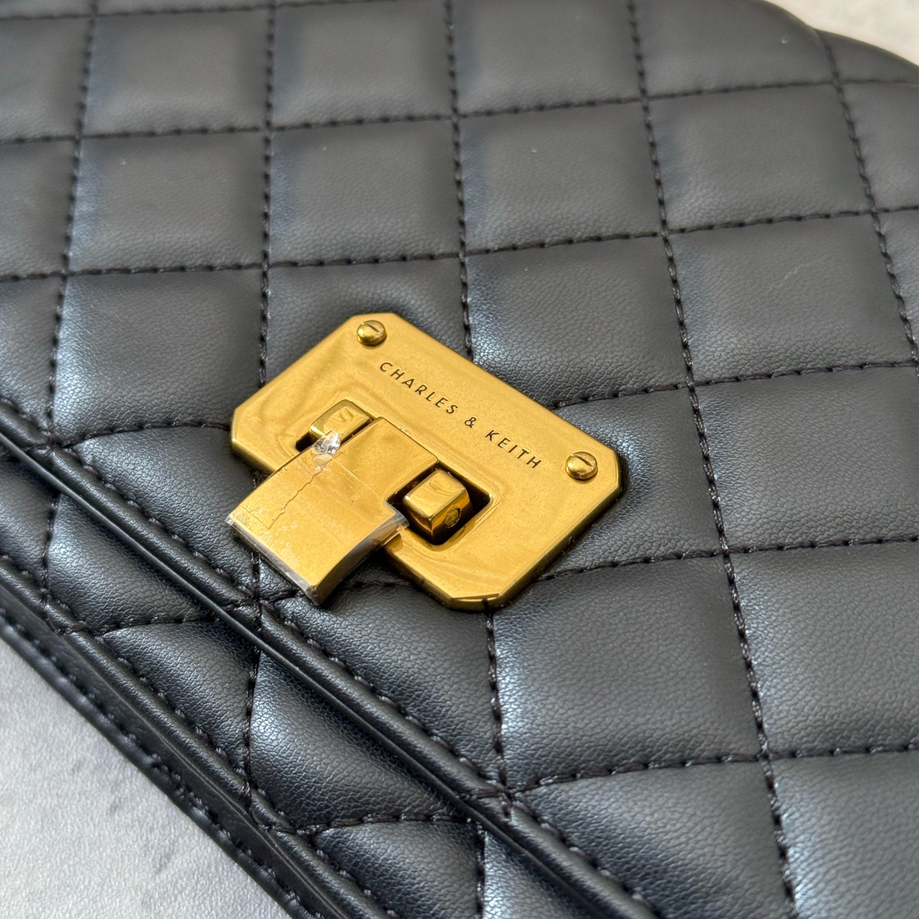 Charles & Keith Cressida Quilted Push-Lock Clutch Bag in black faux leather with gold-tone chain strap and secure push-lock closure.