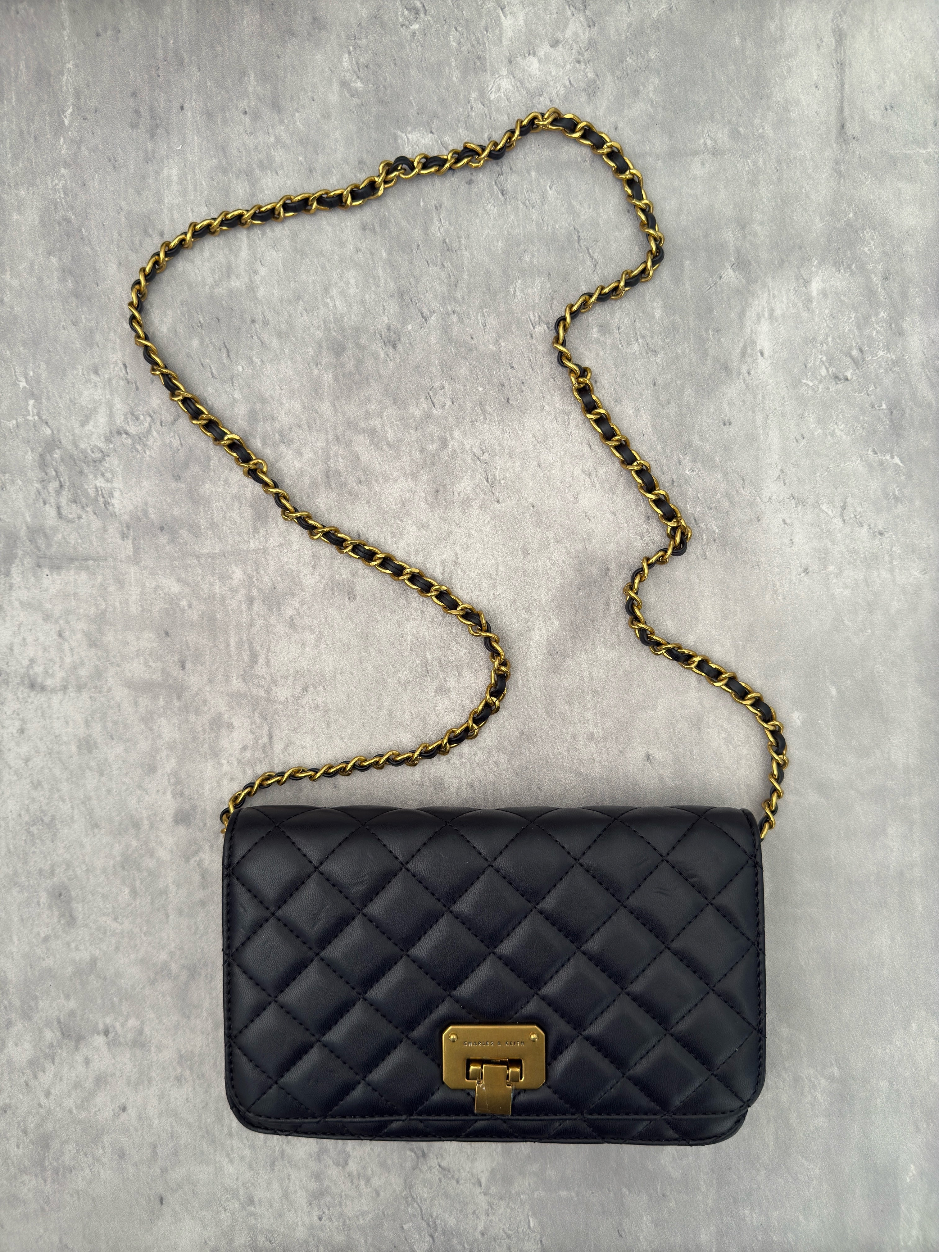 Charles & Keith Cressida Quilted Push-Lock Clutch Bag in black faux leather with gold-tone chain strap and secure push-lock closure.
