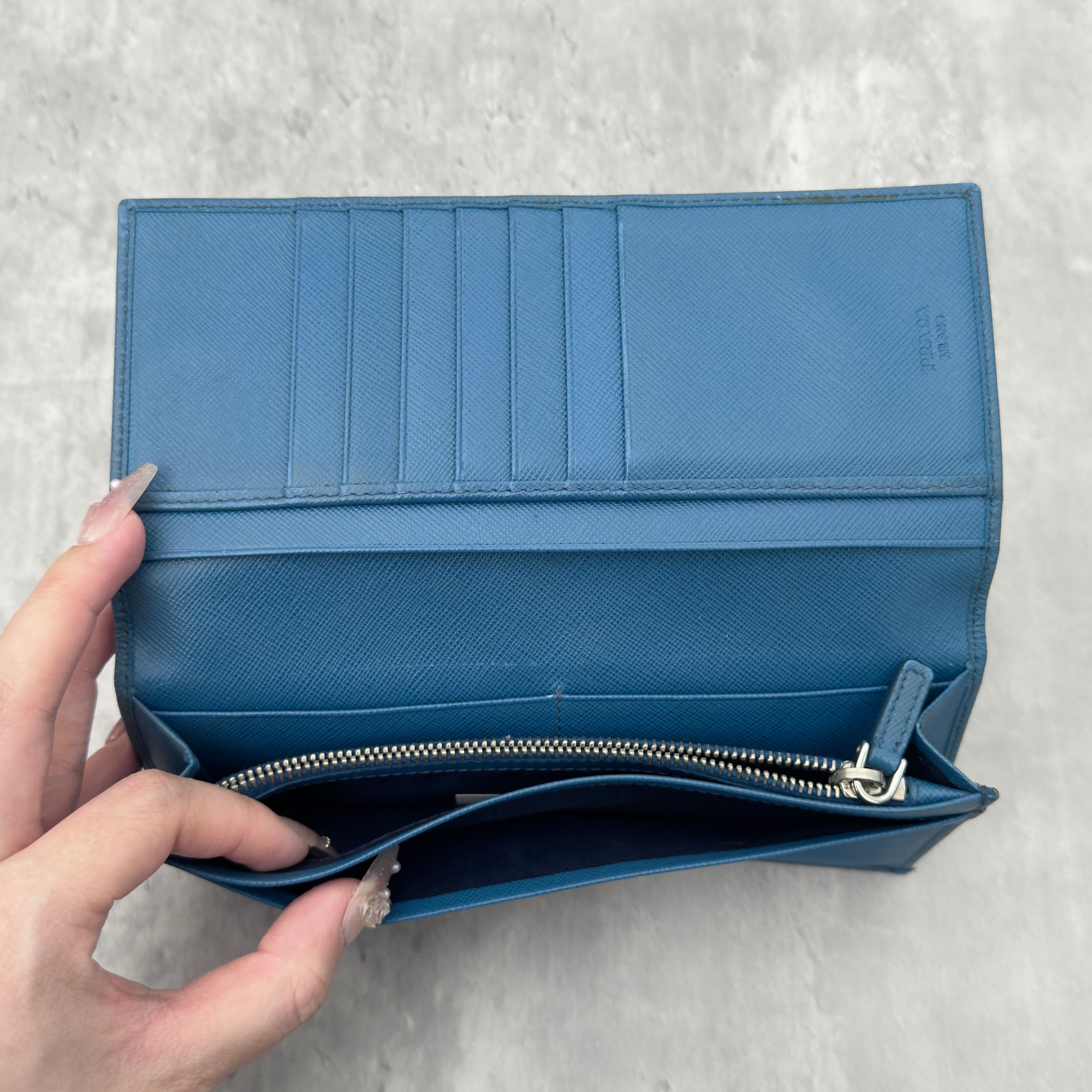 Prada Saffiano Baby Blue Long Wallet in Saffiano leather, featuring an embossed Prada logo, multiple card slots, and a zippered coin compartment.
