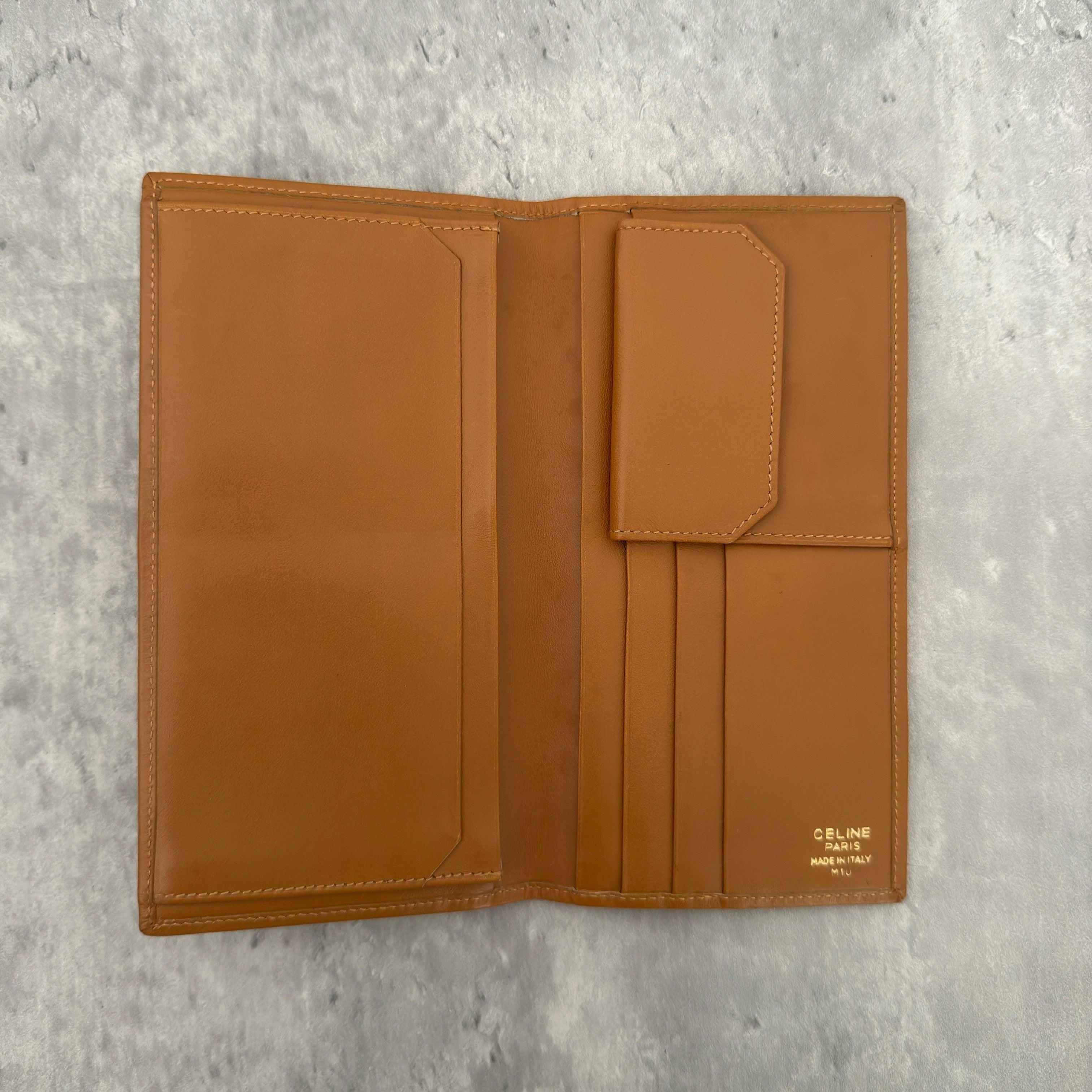 Celine Macadam Triomphe Canvas Long Wallet in brown monogram canvas with tan leather trim, featuring a bifold design with multiple compartments and a snap-button coin pocket.