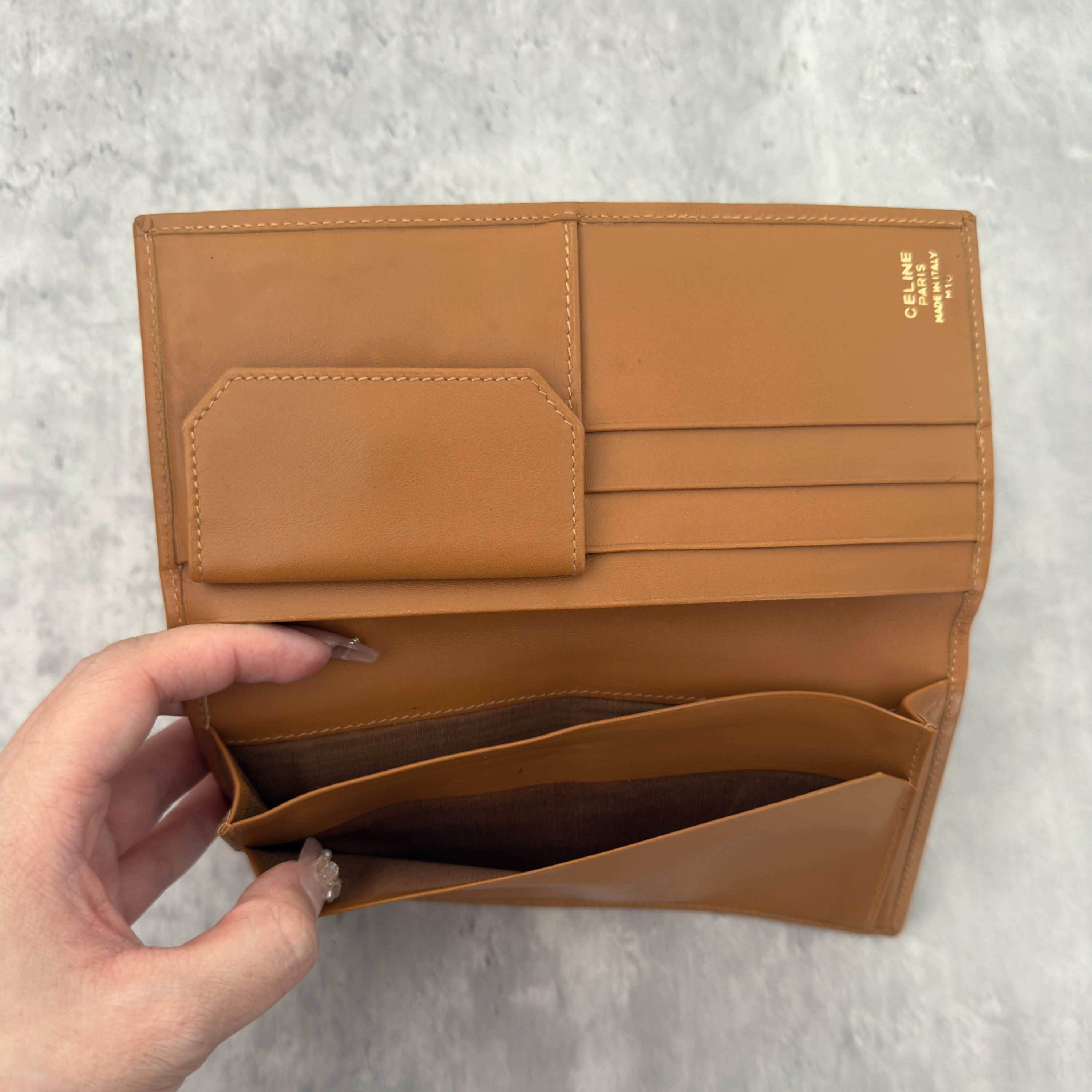 Celine Macadam Triomphe Canvas Long Wallet in brown monogram canvas with tan leather trim, featuring a bifold design with multiple compartments and a snap-button coin pocket.