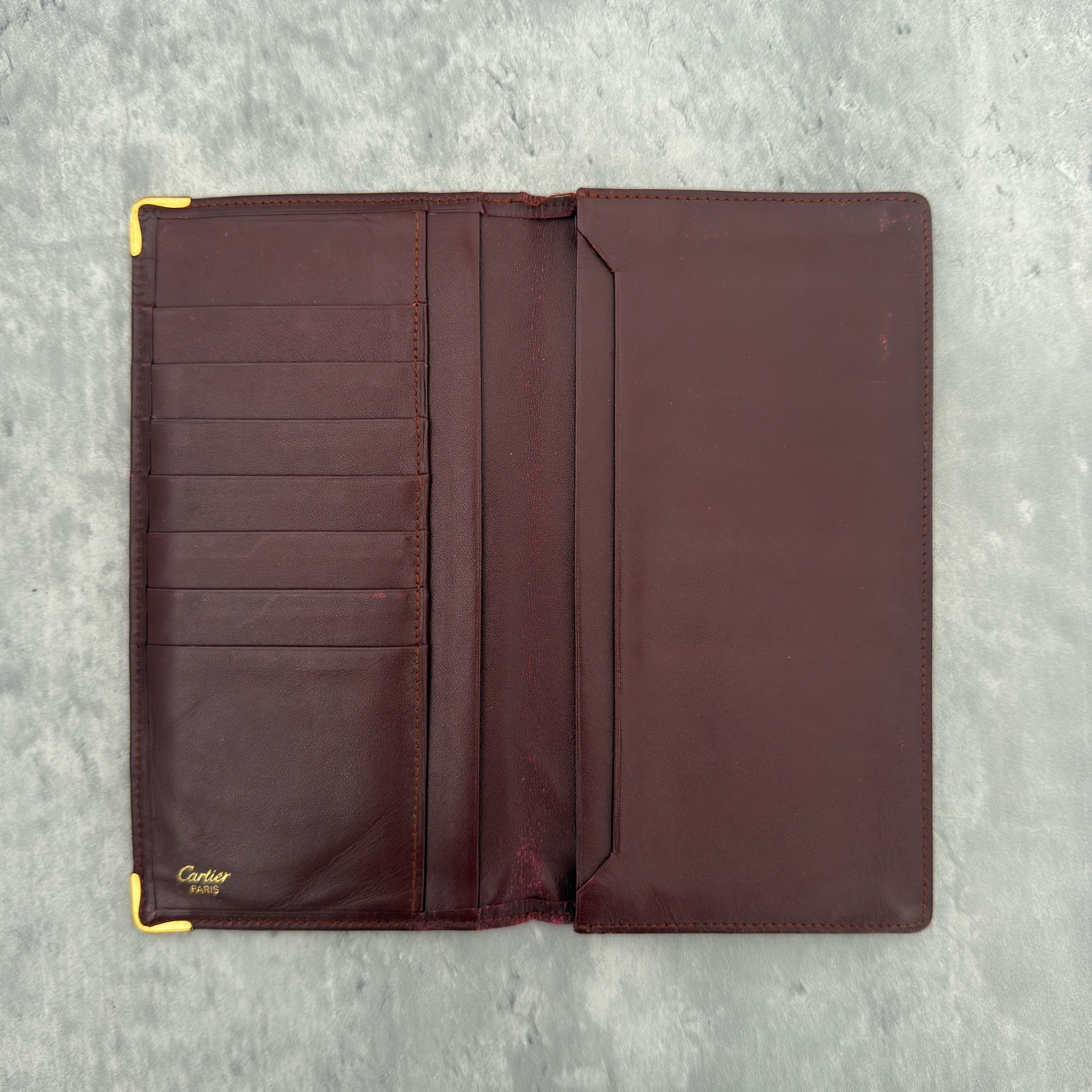Cartier Must De Cartier Burgundy Long Wallet in burgundy leather with gold-tone corner accents and multiple compartments.