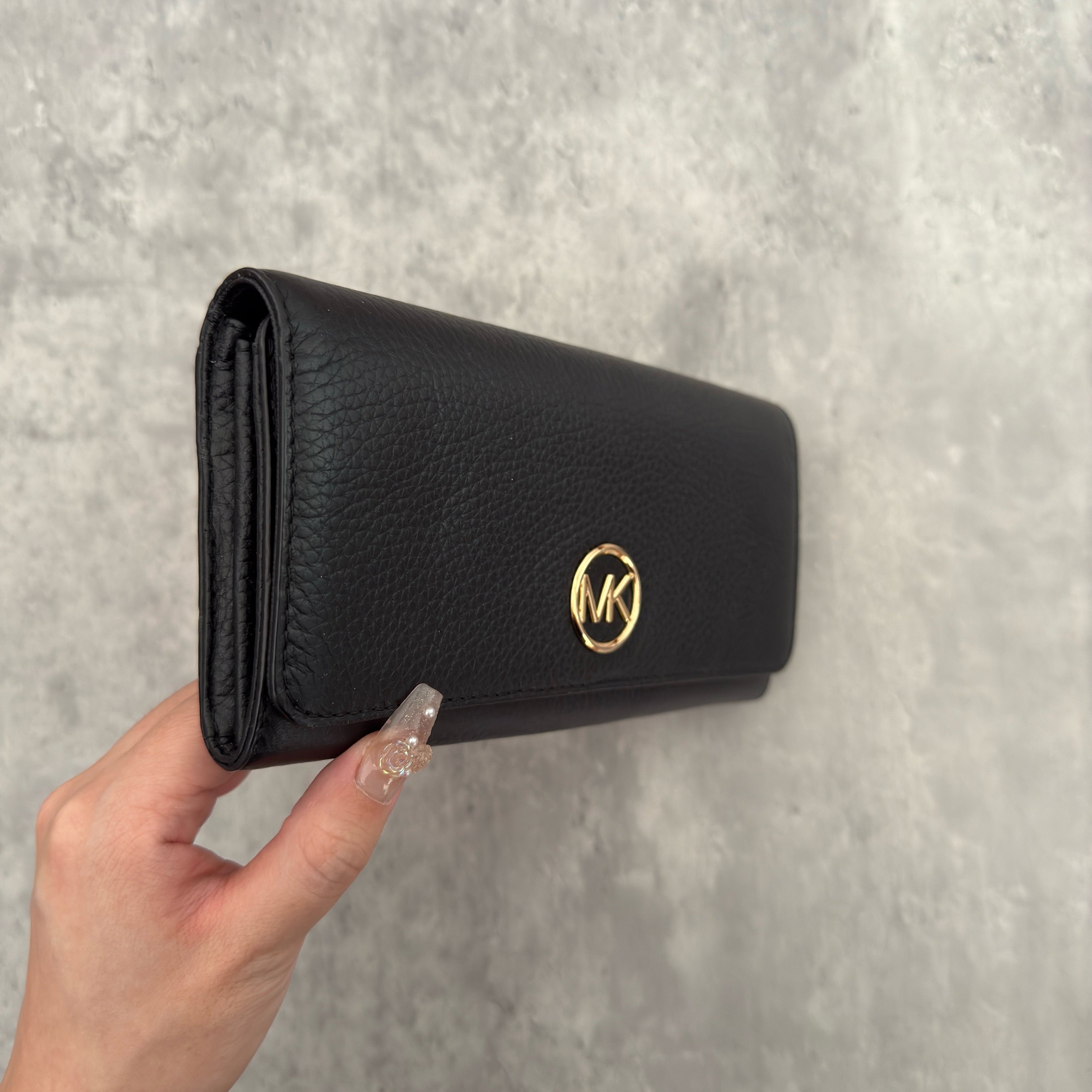 Michael Kors MK Gold Logo Bifold Long Wallet in black pebbled leather, featuring a structured silhouette with a gold-tone MK logo and a snap button closure.