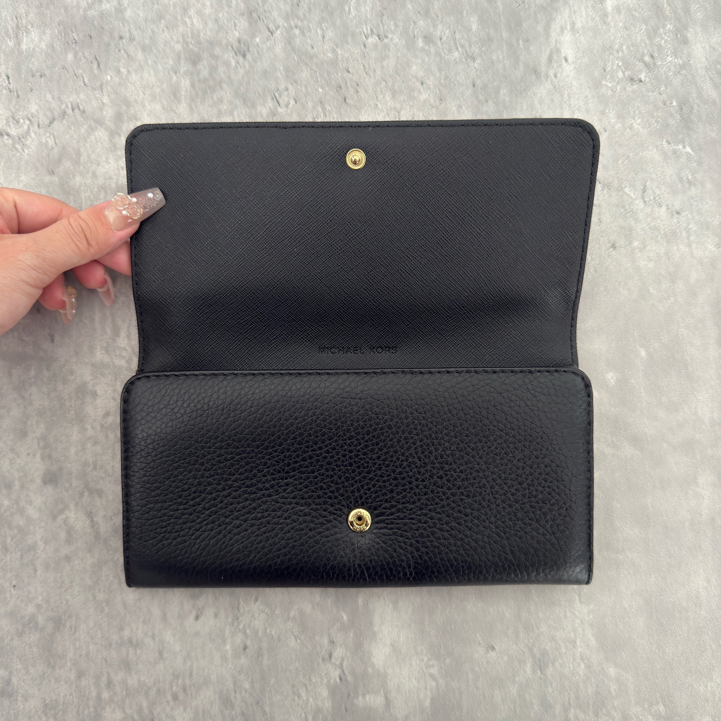 Michael Kors MK Gold Logo Bifold Long Wallet in black pebbled leather, featuring a structured silhouette with a gold-tone MK logo and a snap button closure.