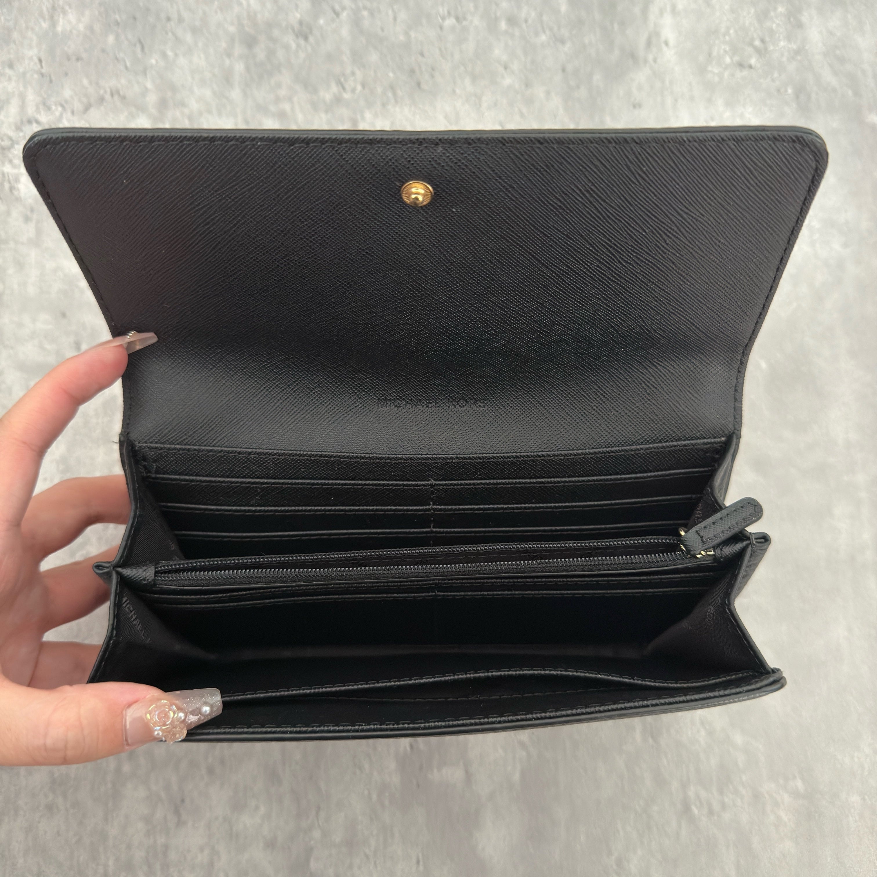 Michael Kors MK Gold Logo Bifold Long Wallet in black pebbled leather, featuring a structured silhouette with a gold-tone MK logo and a snap button closure.