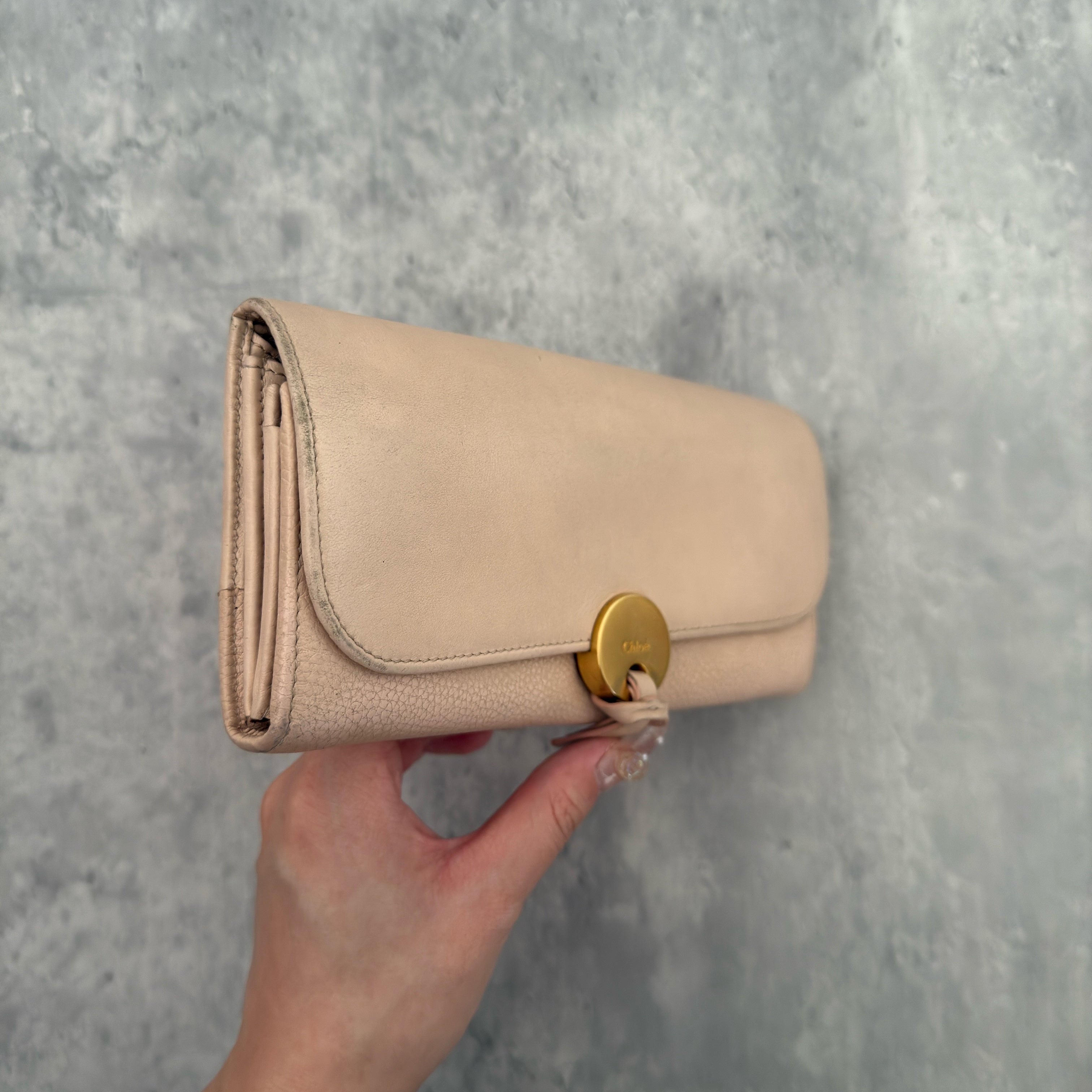 Chloe Grained Smooth Calfskin Indy Long Wallet in Light Pink, featuring a gold-tone circular medallion closure with leather tie detail, crafted from a mix of grained and smooth calfskin leather.