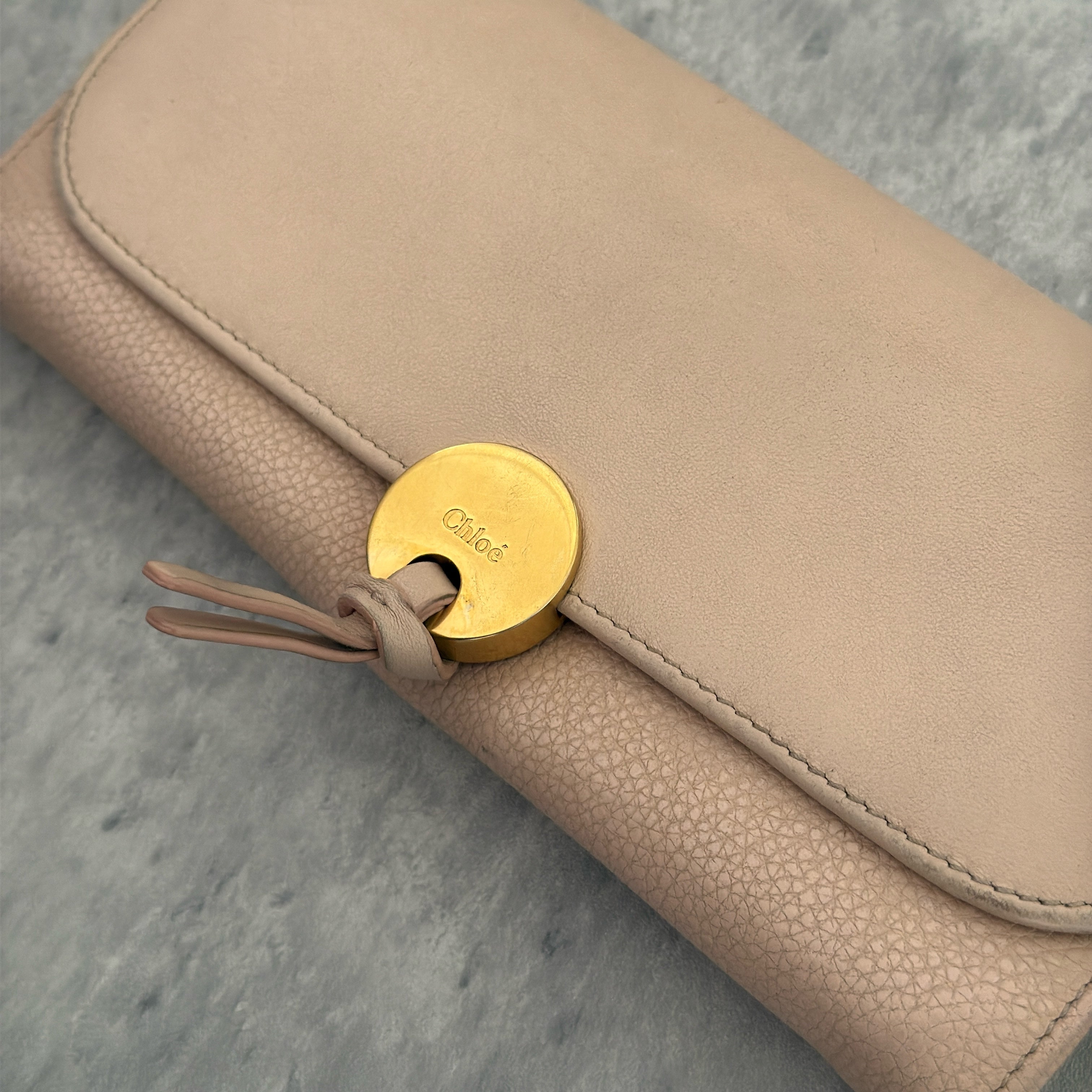 Chloe Grained Smooth Calfskin Indy Long Wallet in Light Pink, featuring a gold-tone circular medallion closure with leather tie detail, crafted from a mix of grained and smooth calfskin leather.