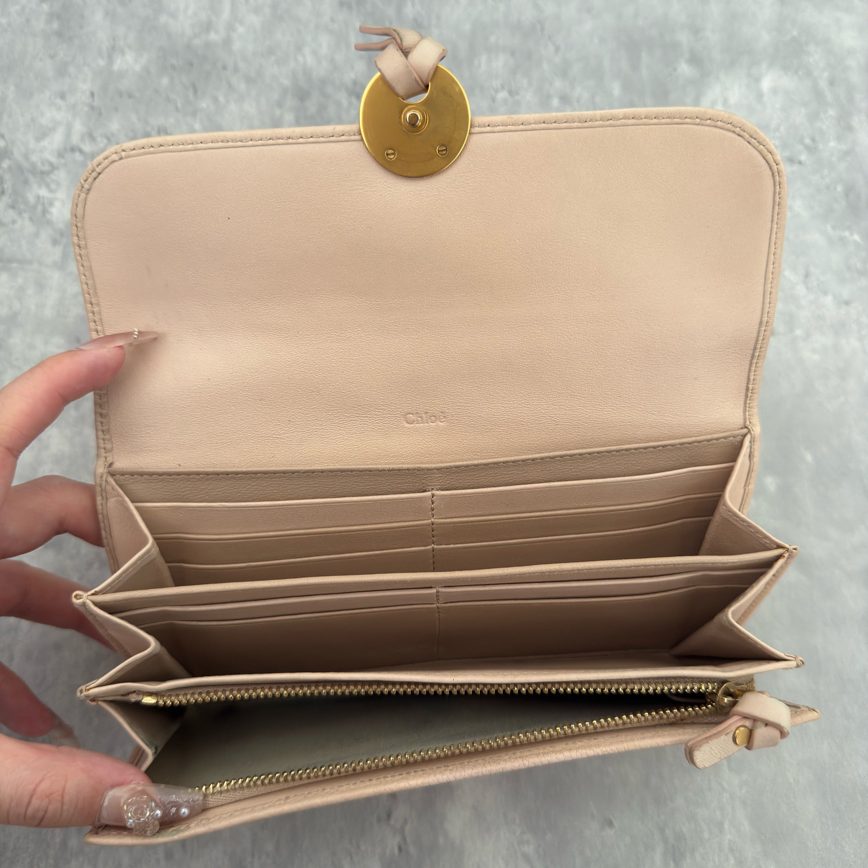 Chloe Grained Smooth Calfskin Indy Long Wallet in Light Pink, featuring a gold-tone circular medallion closure with leather tie detail, crafted from a mix of grained and smooth calfskin leather.