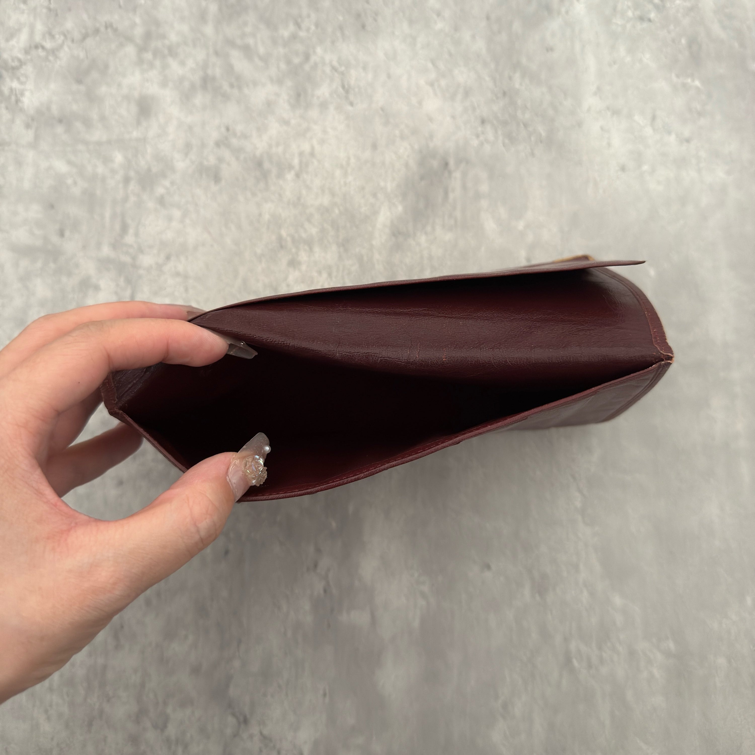 Cartier Must De Cartier Long Wallet in burgundy leather with embossed logo, gold-tone corner accents, and multiple compartments for organised storage.