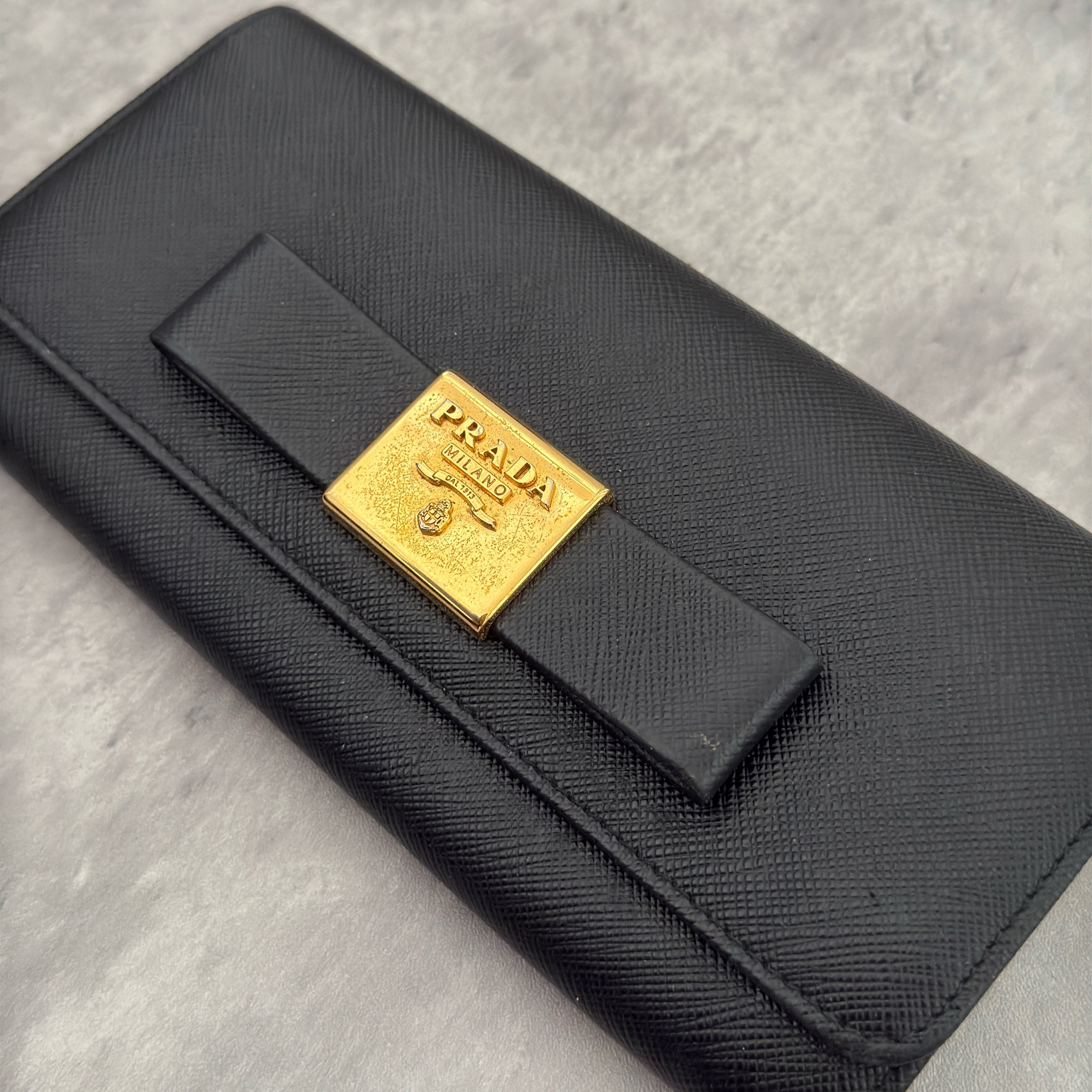 Prada Milano Black Saffiano Leather Ribbon Bow Long Wallet, crafted from textured black Saffiano leather with a gold-tone logo plaque and ribbon bow detail.