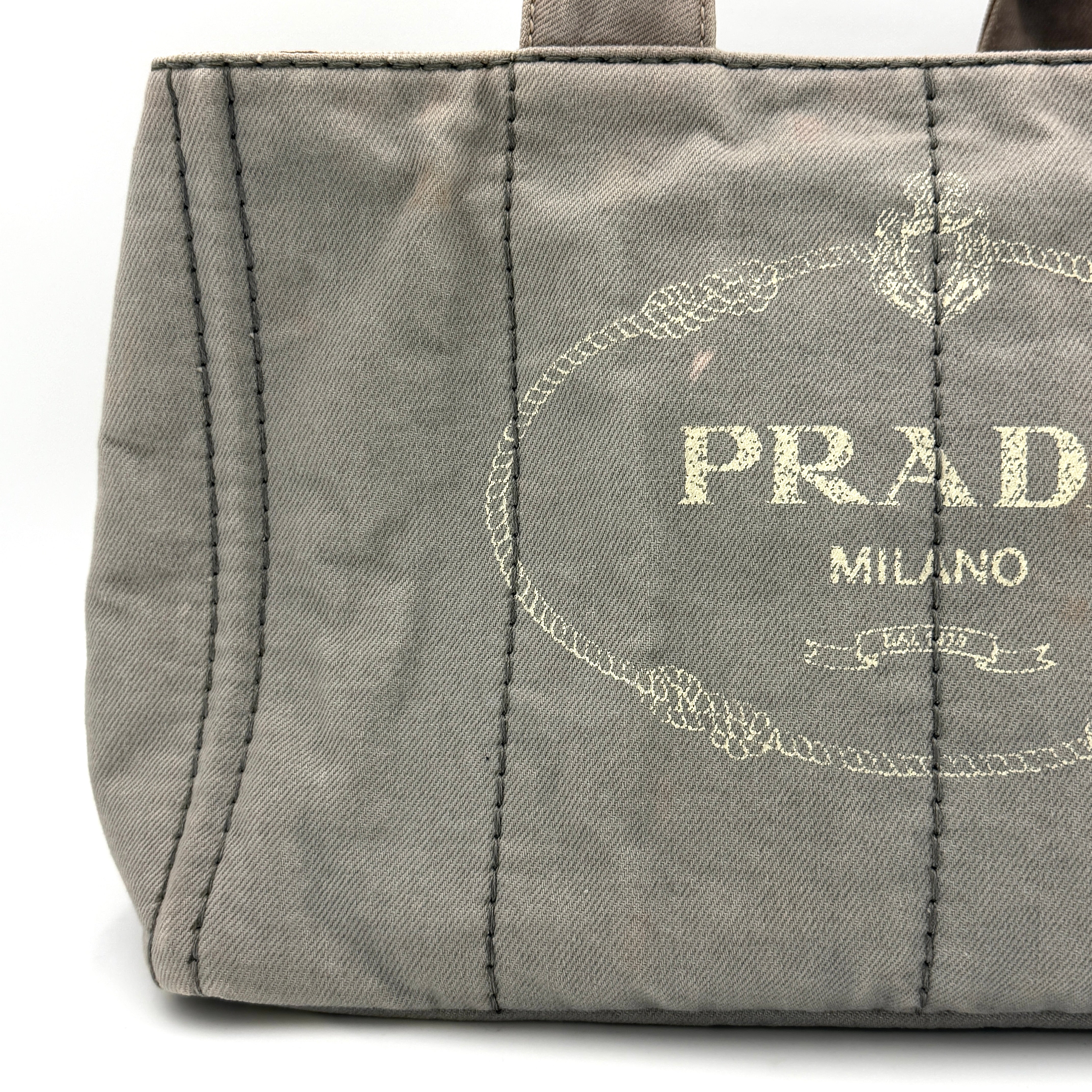 Prada Canapa Tote Bag in grey canvas with rope logo motif and dual top handles against a plain background.