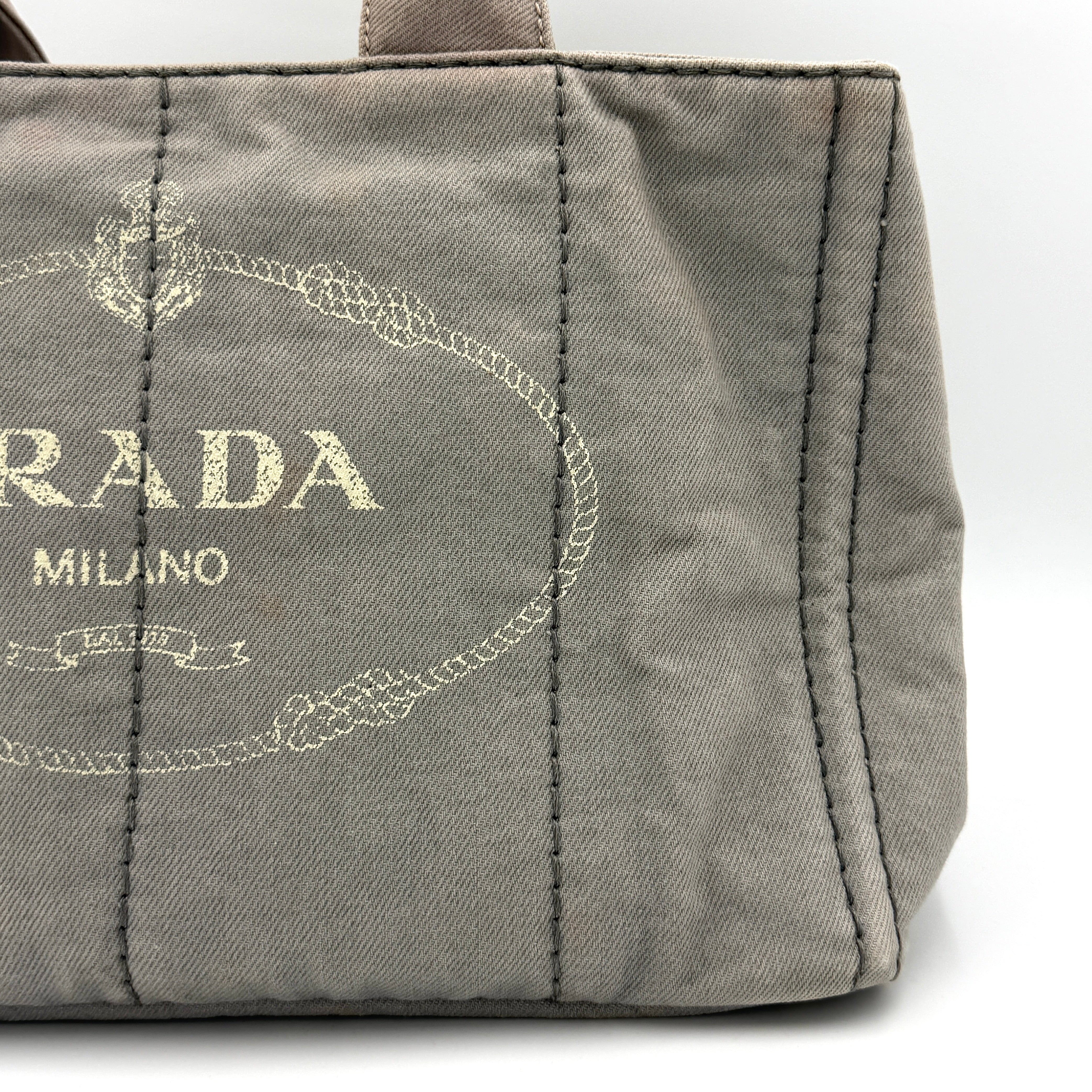 Prada Canapa Tote Bag in grey canvas with rope logo motif and dual top handles against a plain background.