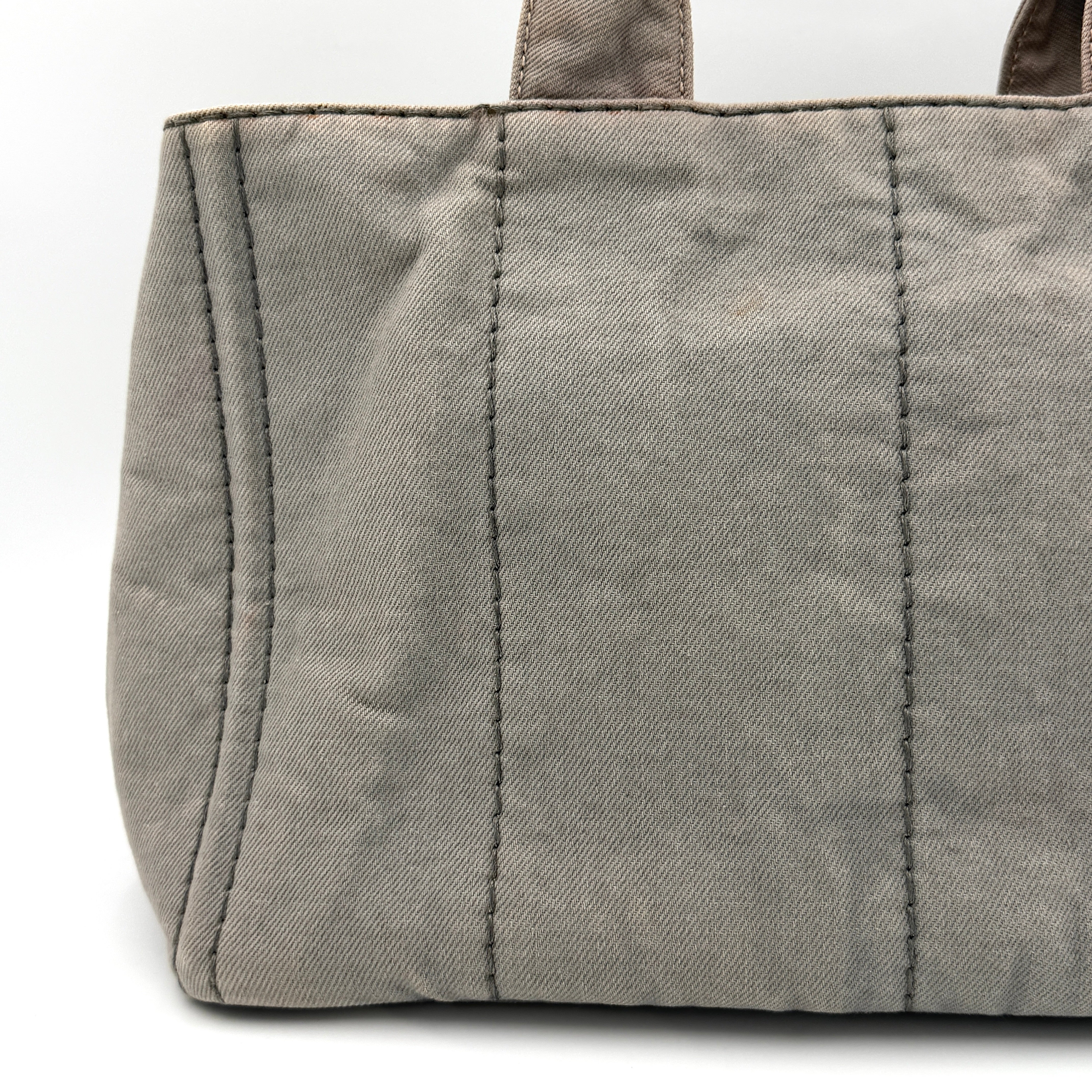 Prada Canapa Tote Bag in grey canvas with rope logo motif and dual top handles against a plain background.