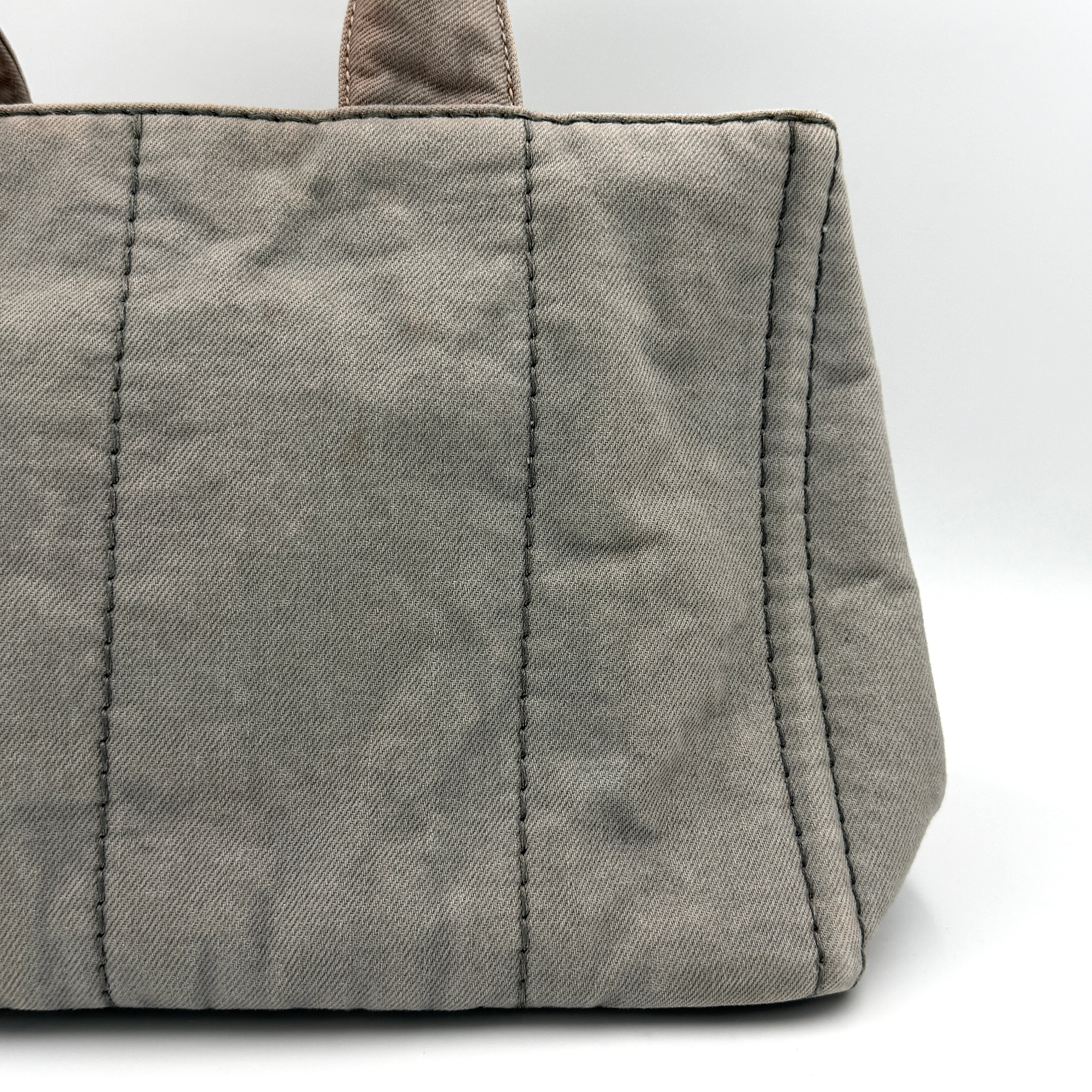 Prada Canapa Tote Bag in grey canvas with rope logo motif and dual top handles against a plain background.