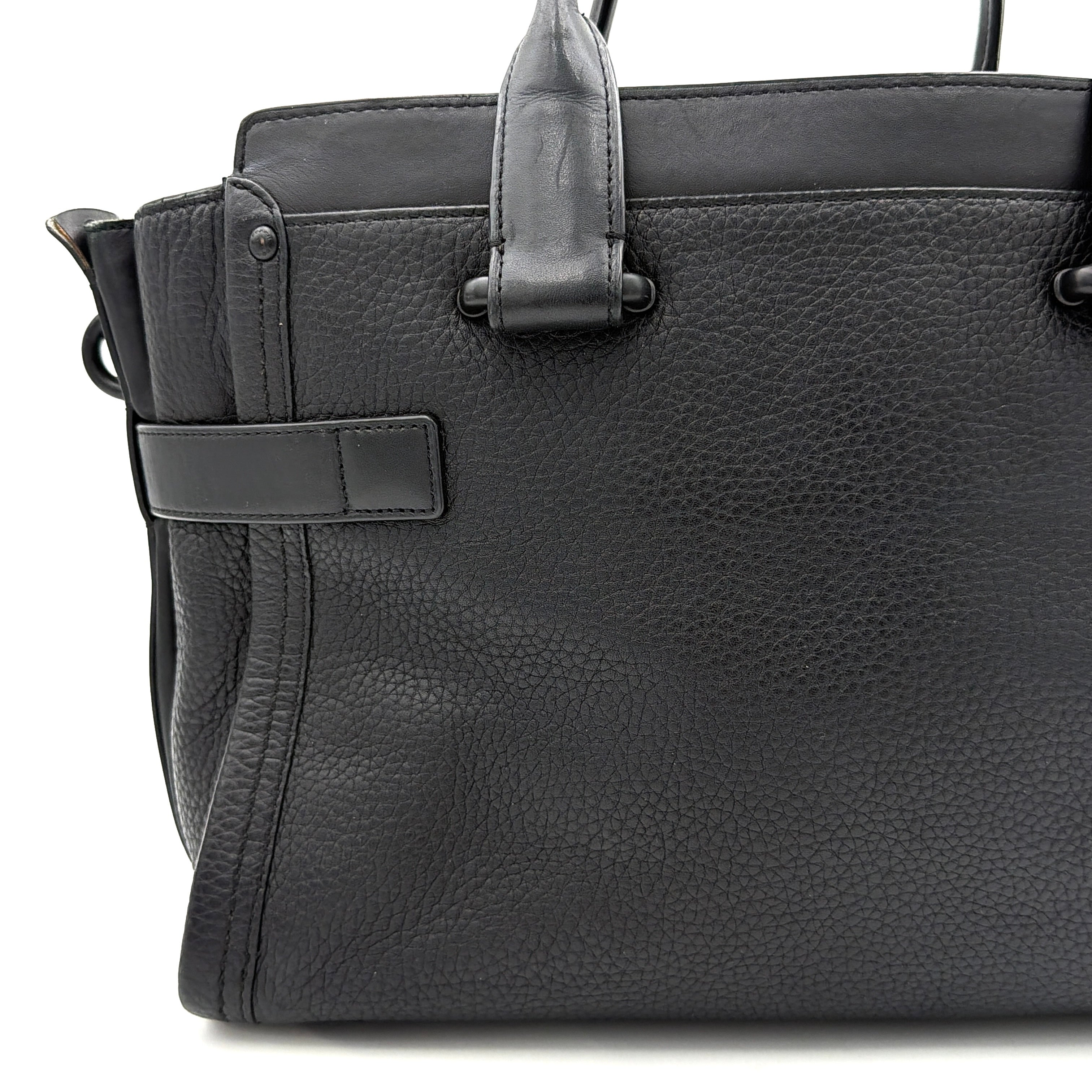 Coach Swagger Carryall handbag in black pebbled leather with matte black hardware and a vibrant orange butterfly charm.