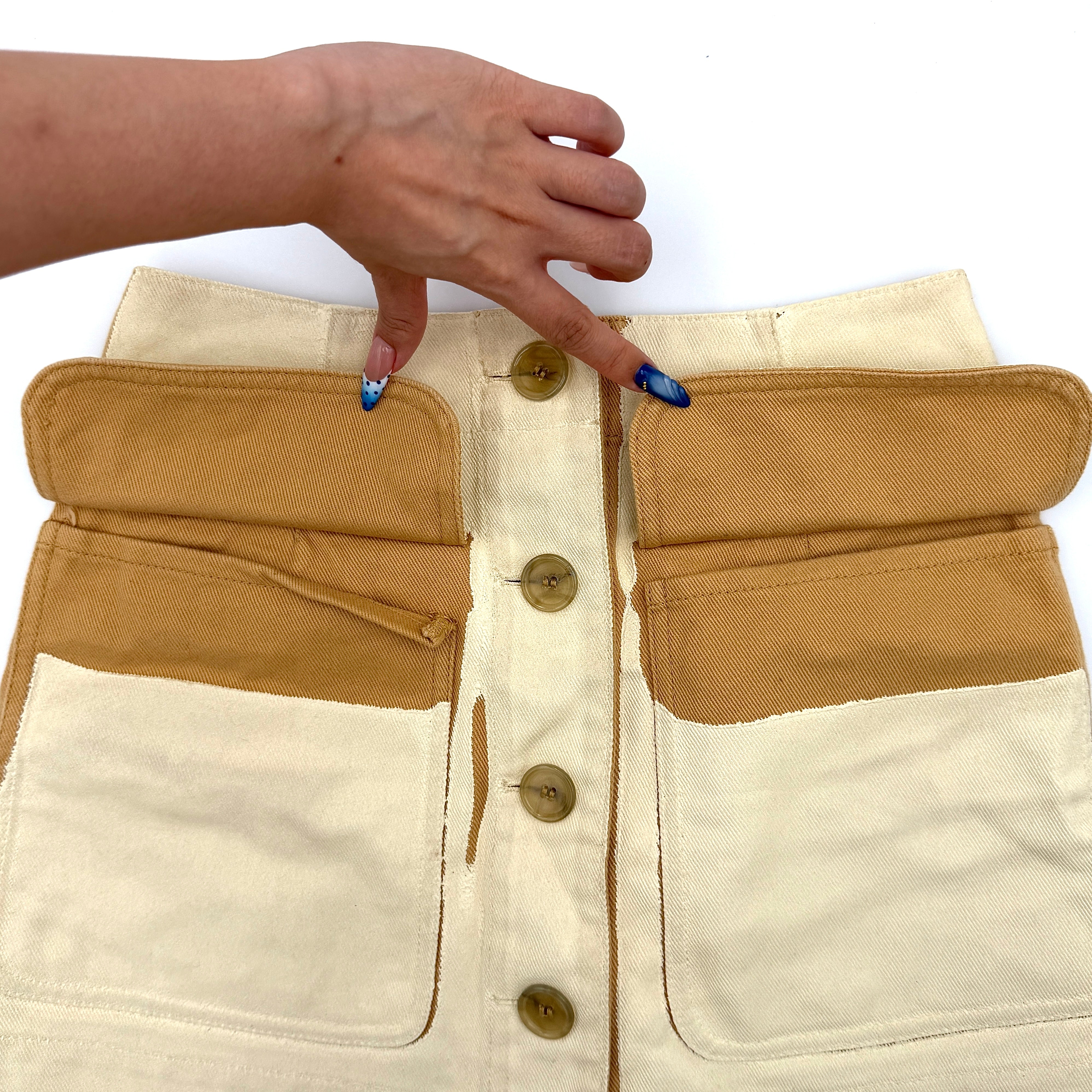 Acne Studios cream and tan cotton drill mini skirt with oversized flap pockets and front button closure, styled flat.