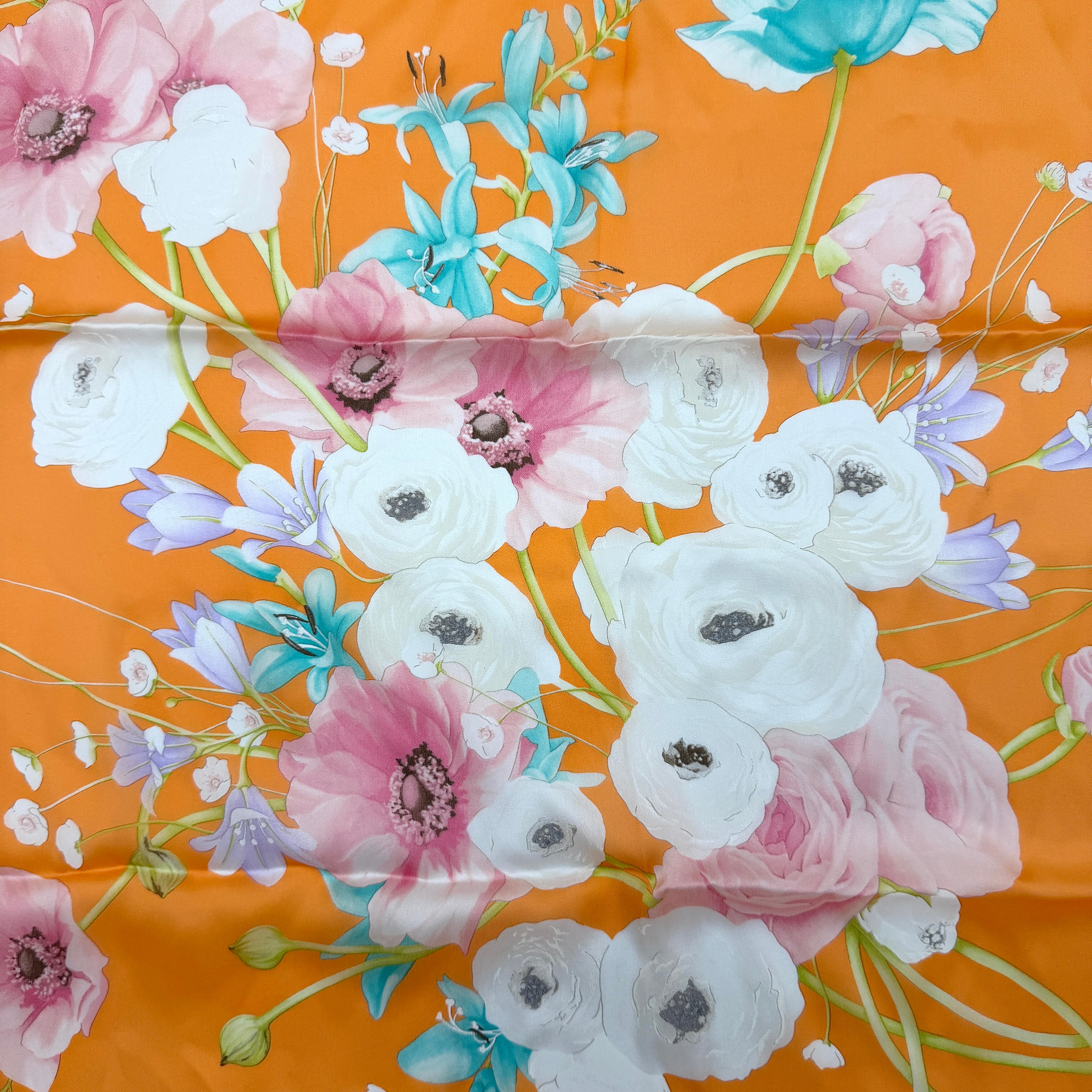 An orange Salvatore Ferragamo silk scarf with pastel floral print displayed in a gentle drape.