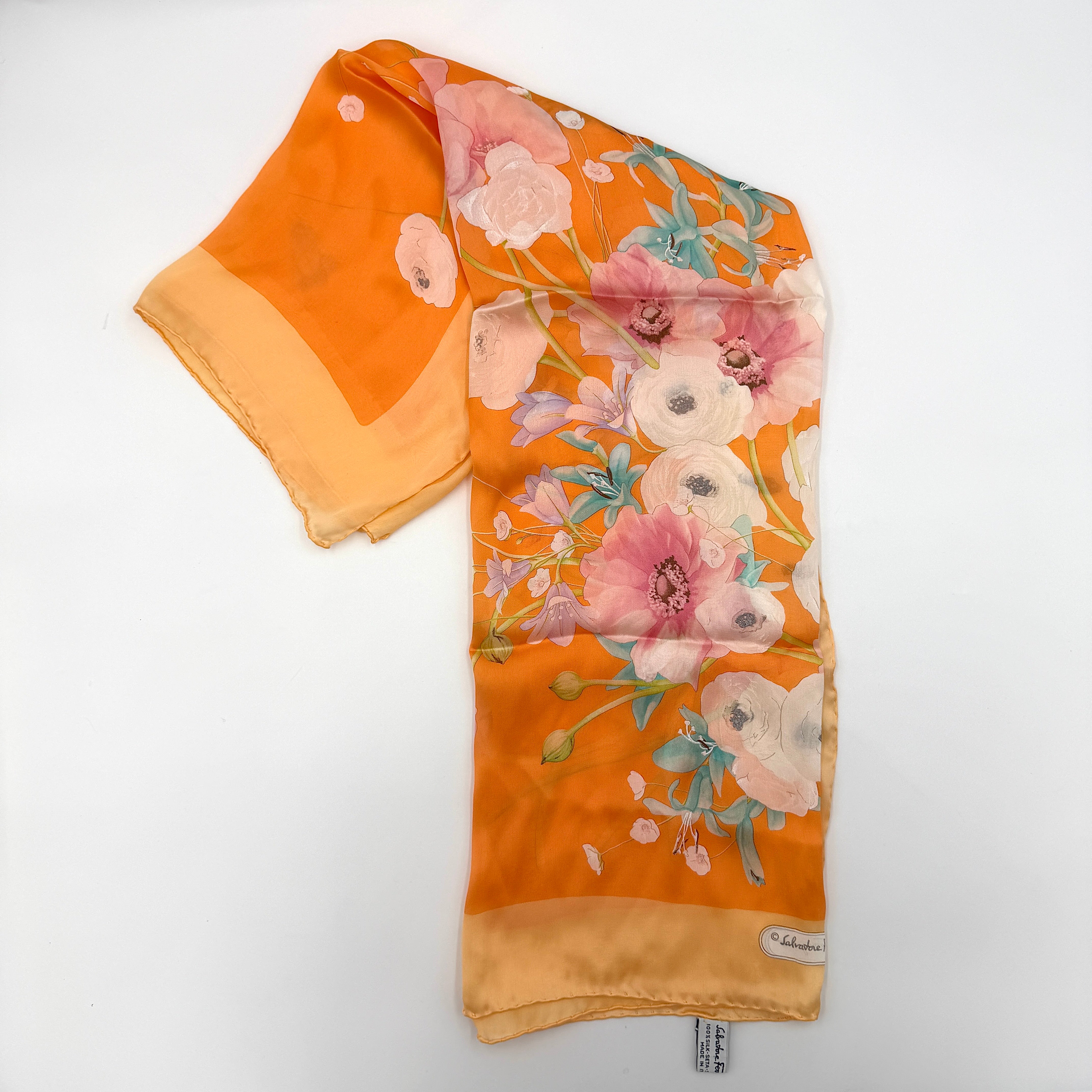 An orange Salvatore Ferragamo silk scarf with pastel floral print displayed in a gentle drape.