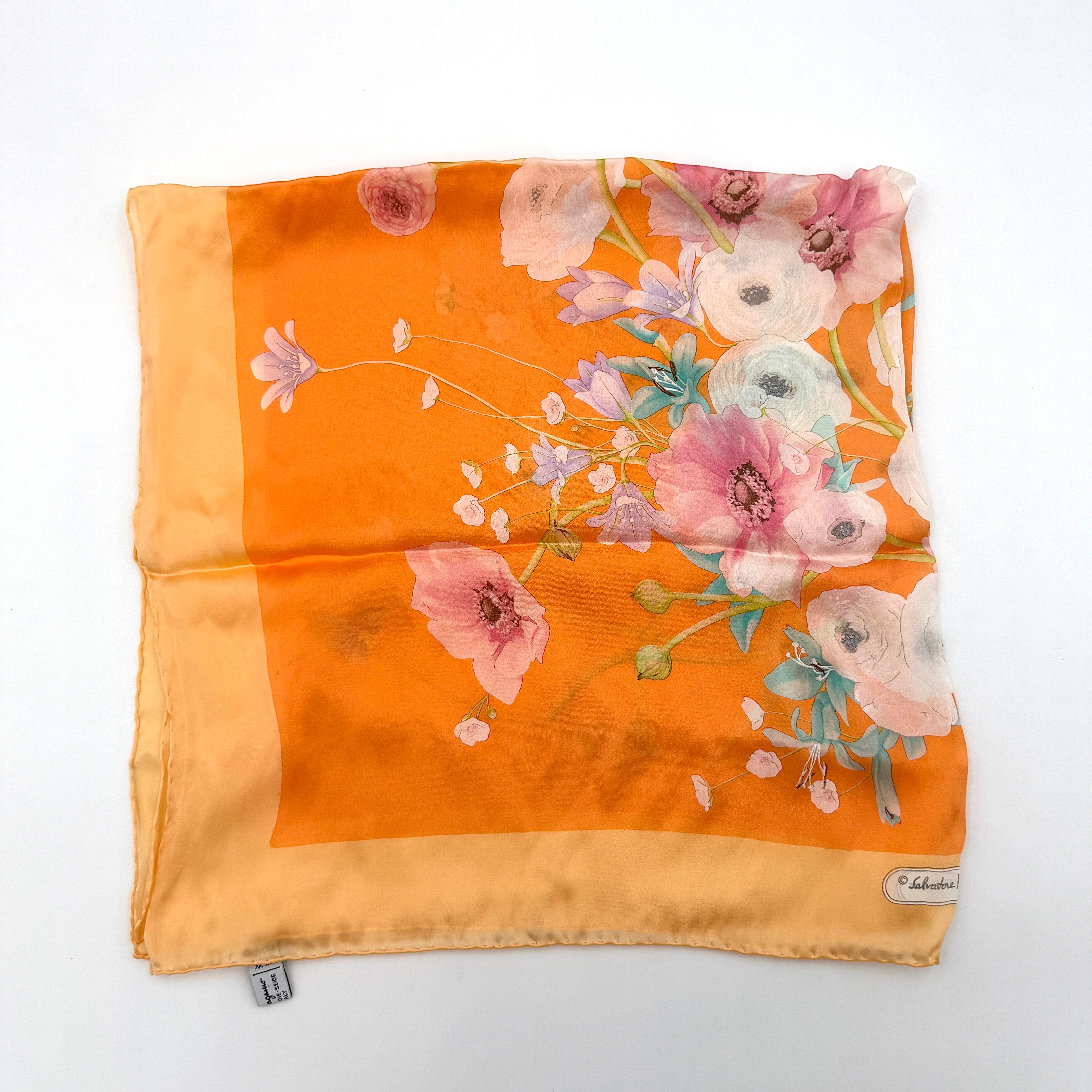 An orange Salvatore Ferragamo silk scarf with pastel floral print displayed in a gentle drape.