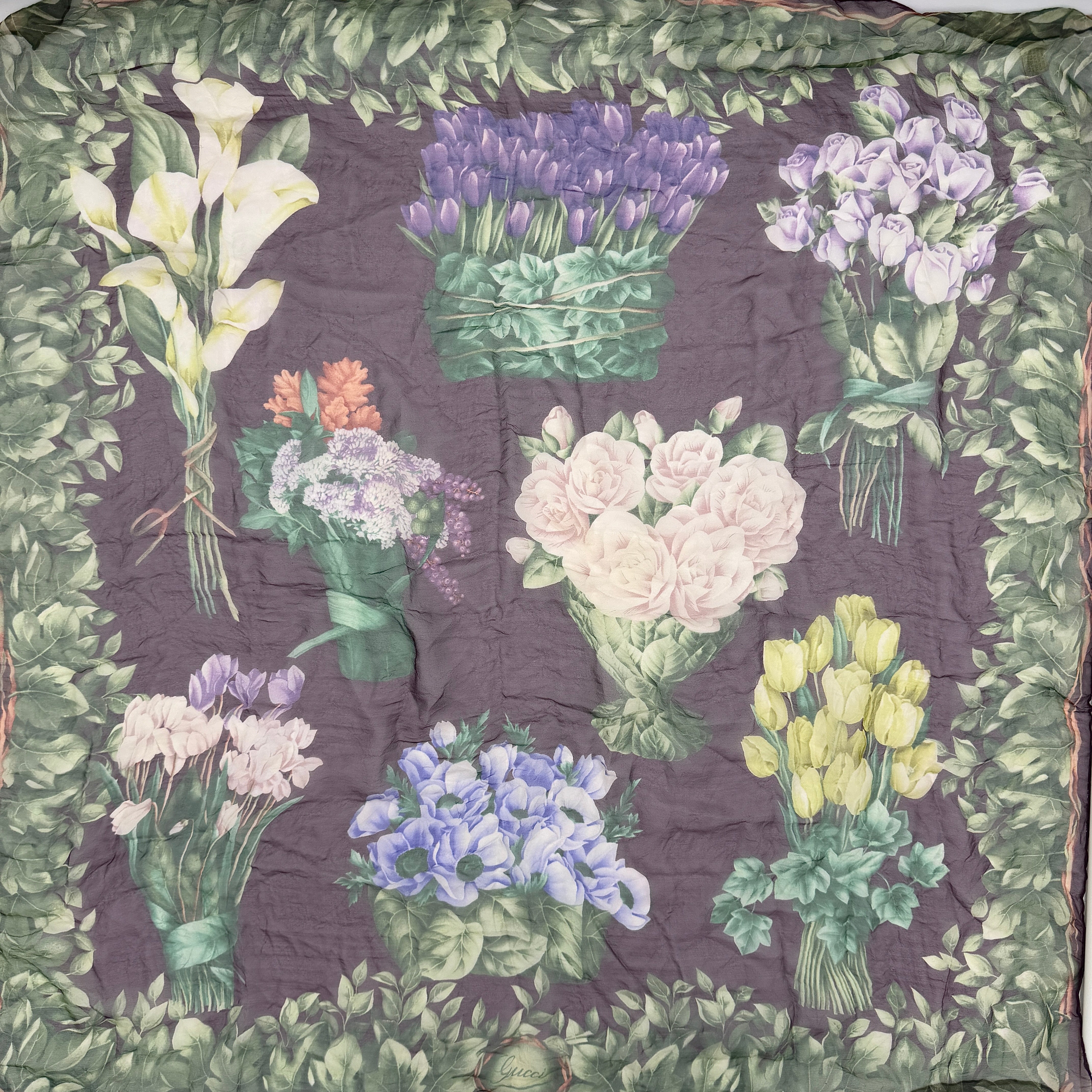 Gucci silk scarf adorned with artistic multicolour floral bouquets and leafy green border, elegantly draped to showcase its lightweight, sheer texture.