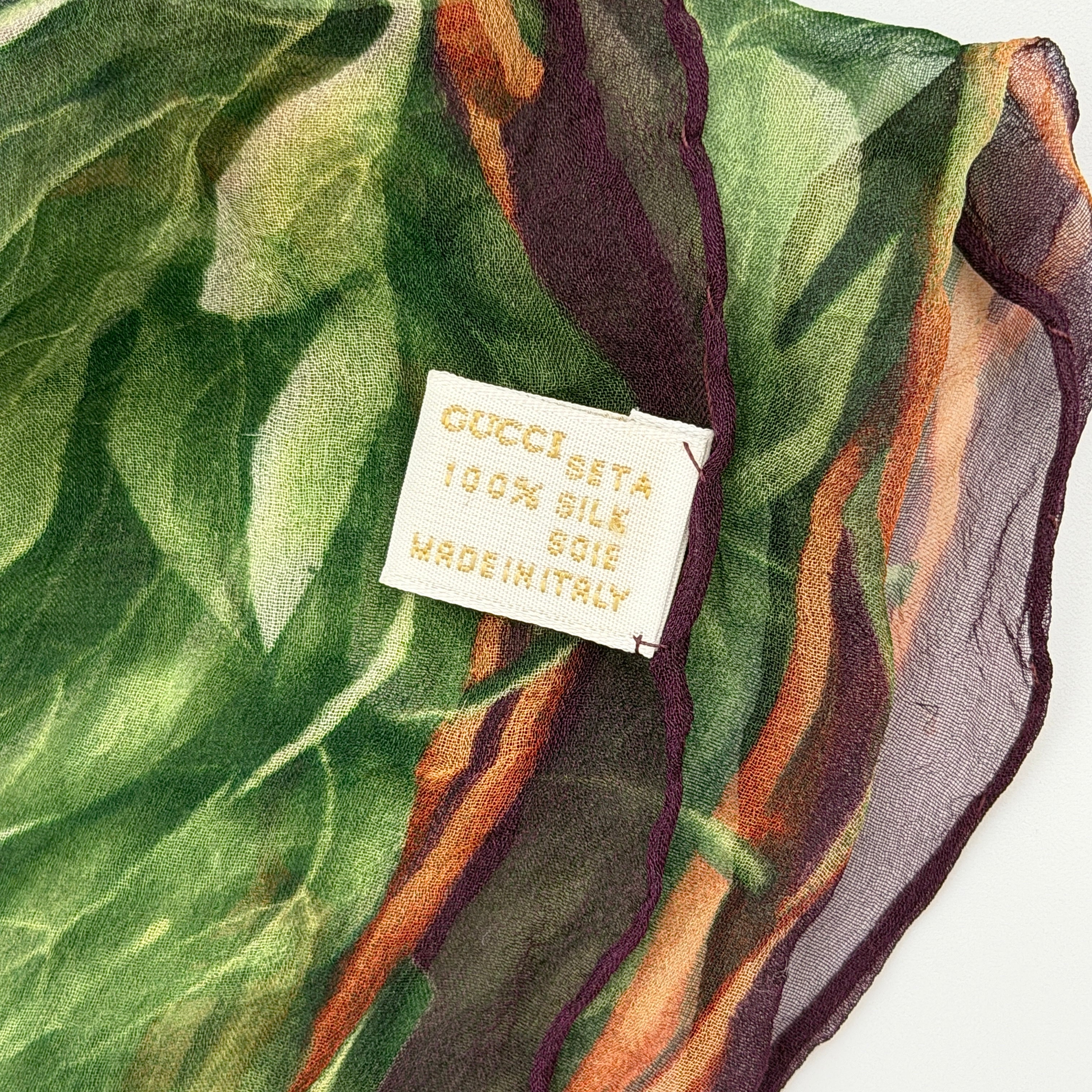 Gucci silk scarf adorned with artistic multicolour floral bouquets and leafy green border, elegantly draped to showcase its lightweight, sheer texture.