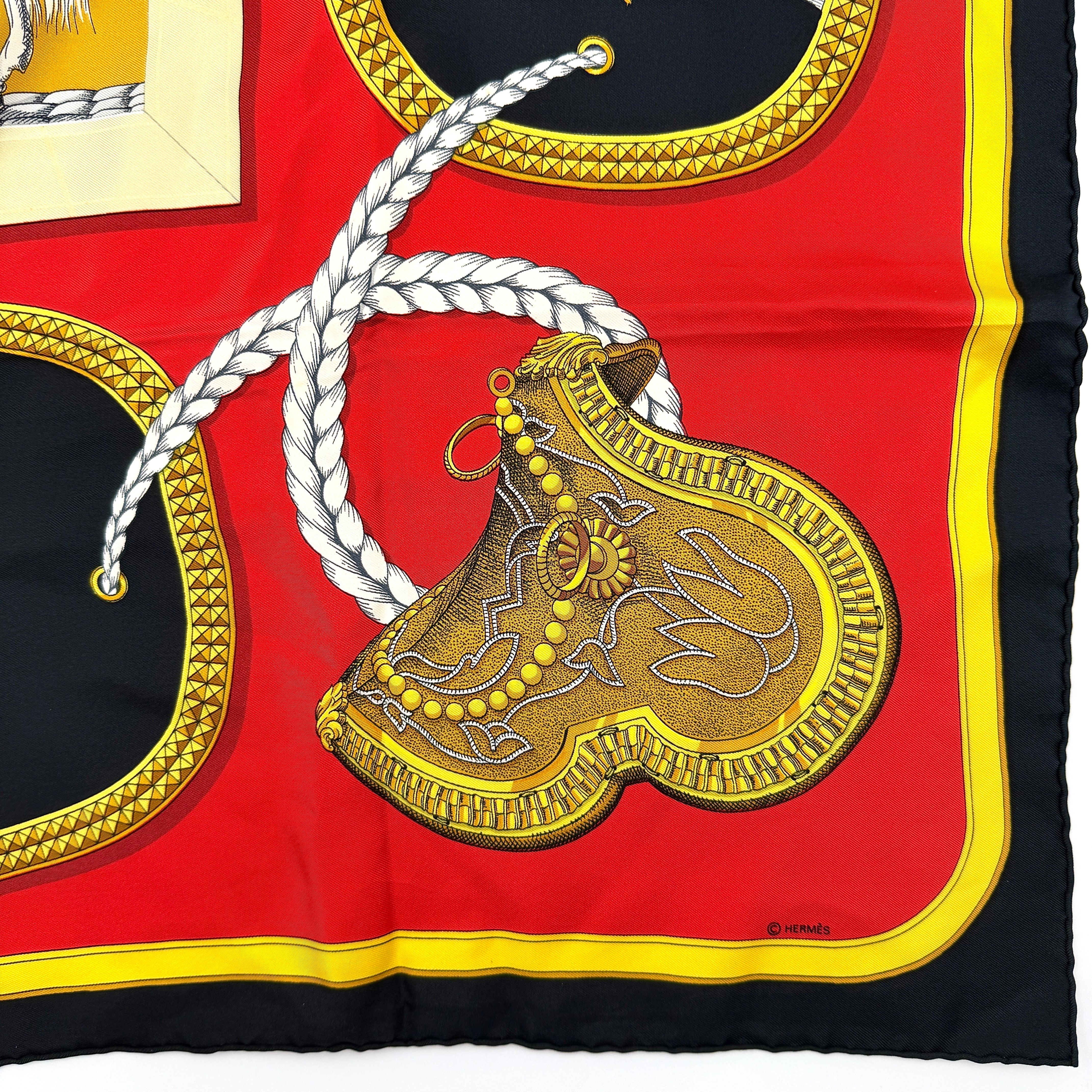 Hermès Grand Apparat silk scarf, featuring an ornate equestrian motif in rich red, gold, and black, elegantly folded to showcase its intricate print.