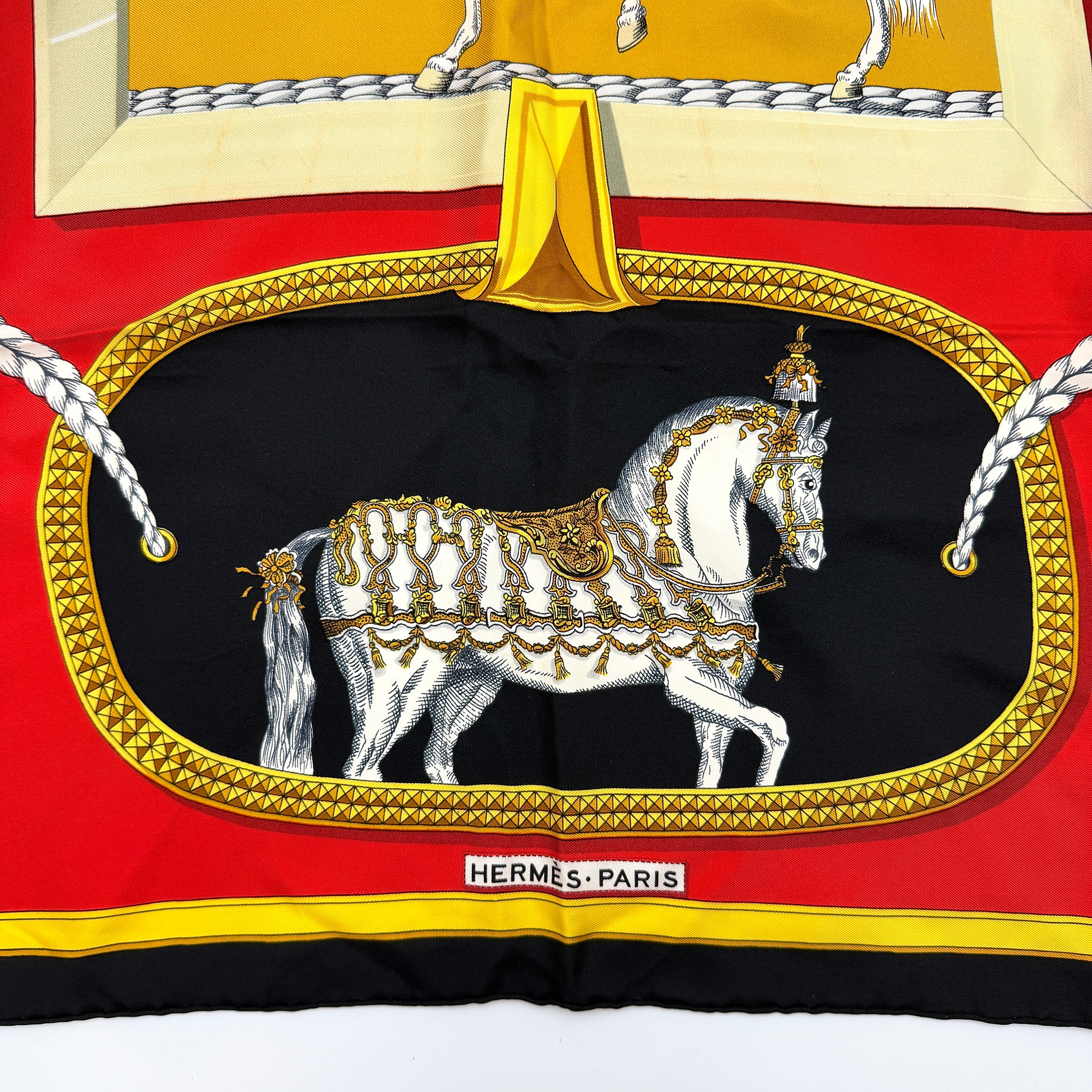 Hermès Grand Apparat silk scarf, featuring an ornate equestrian motif in rich red, gold, and black, elegantly folded to showcase its intricate print.