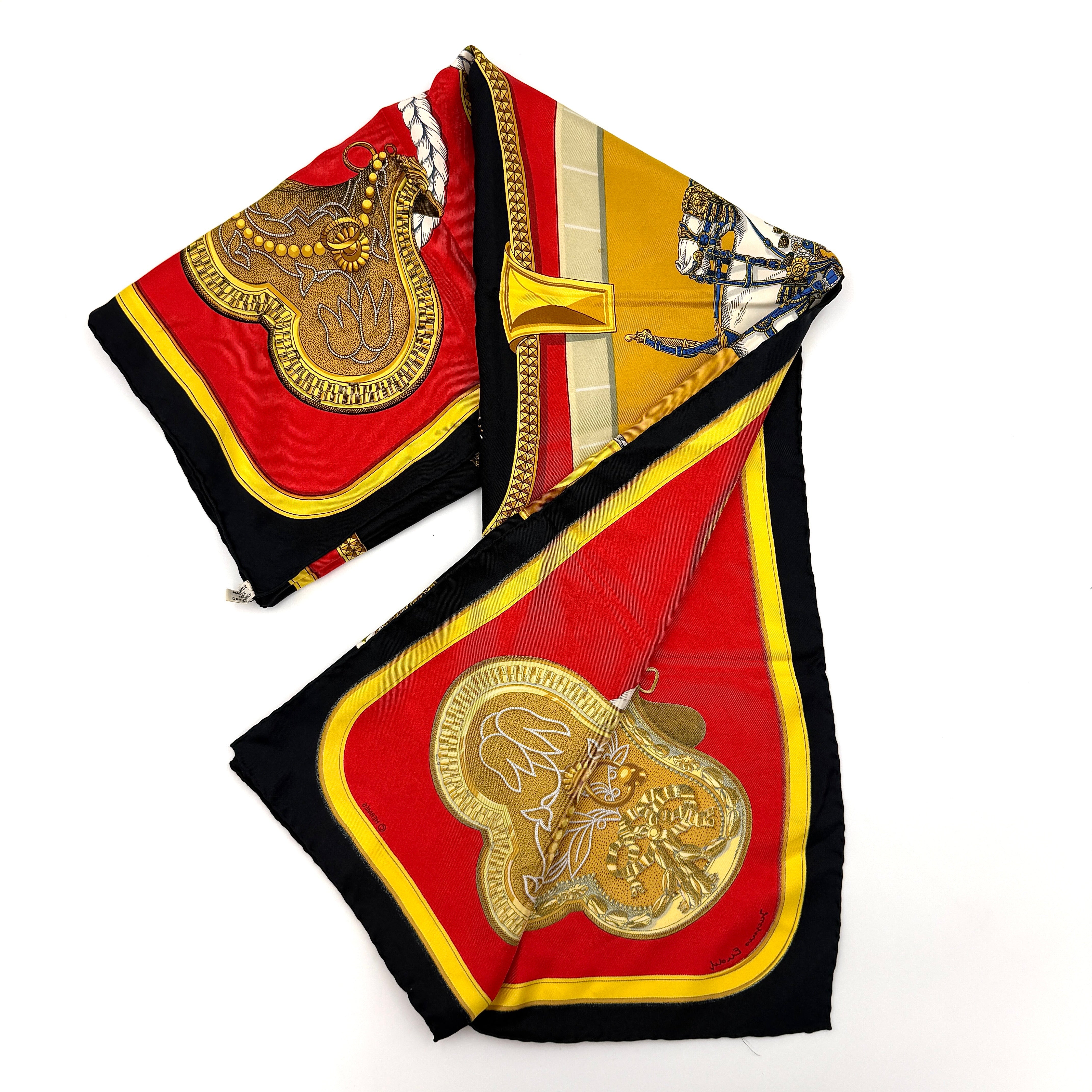 Hermès Grand Apparat silk scarf, featuring an ornate equestrian motif in rich red, gold, and black, elegantly folded to showcase its intricate print.