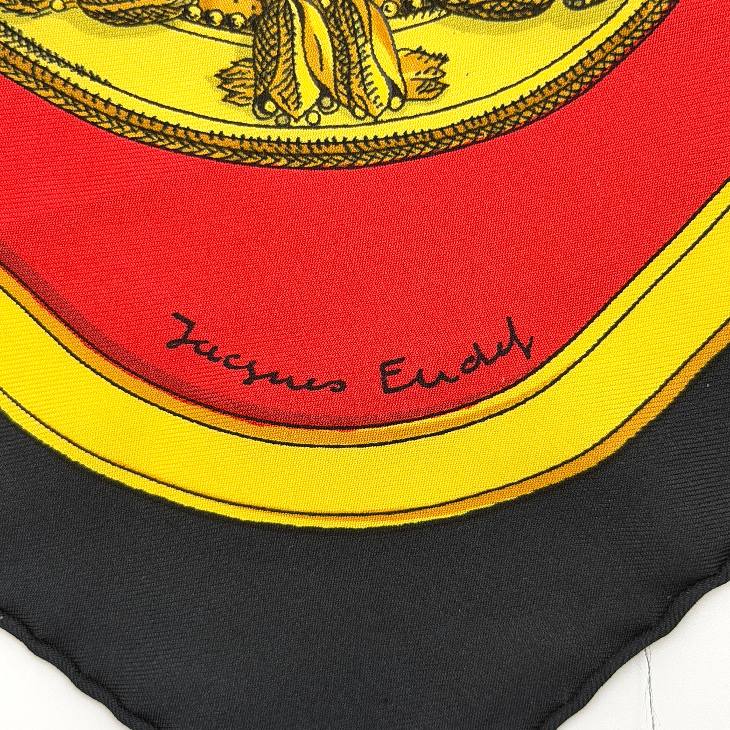 Hermès Grand Apparat silk scarf, featuring an ornate equestrian motif in rich red, gold, and black, elegantly folded to showcase its intricate print.