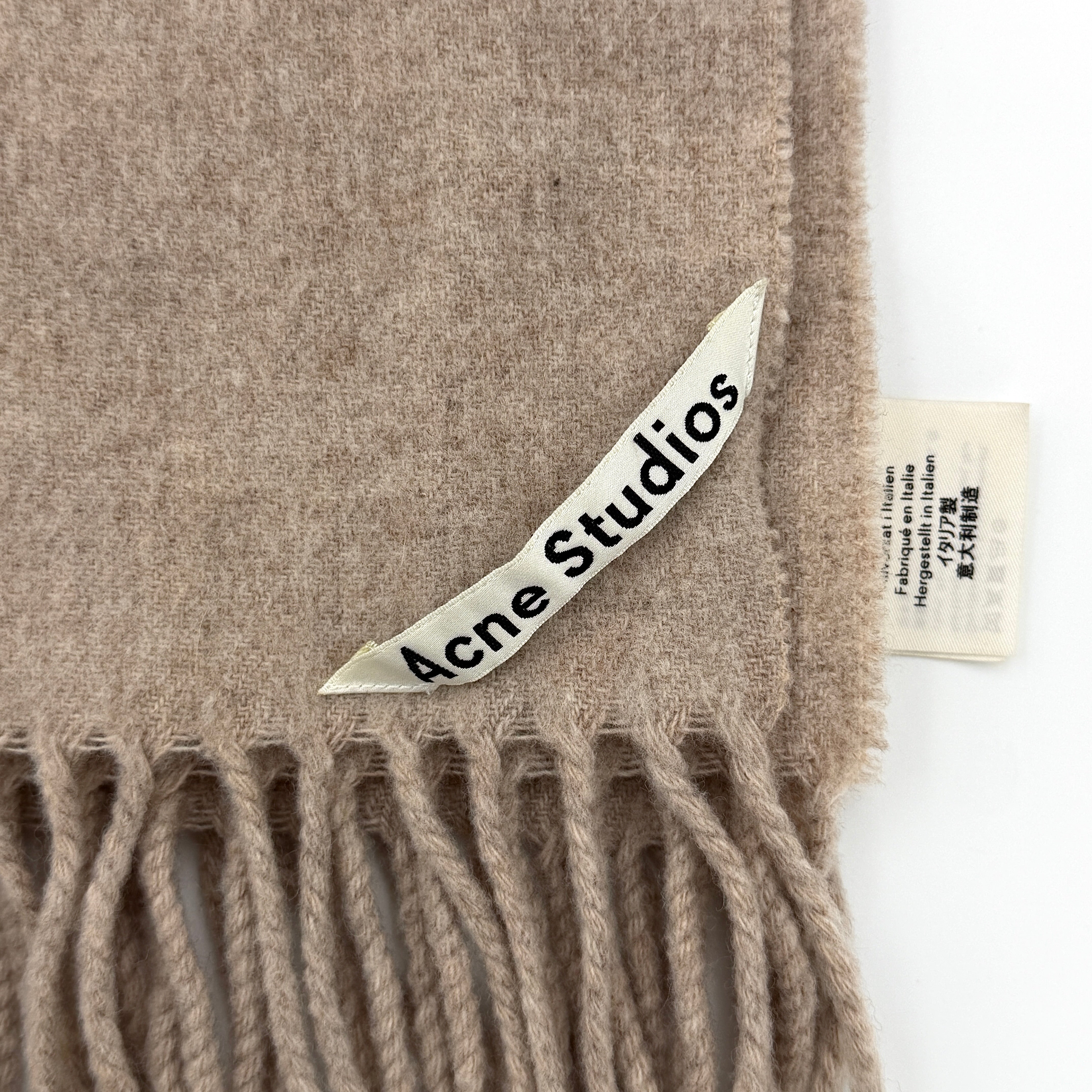 Acne Studios wool scarf in soft light brown with a fringed edge and signature label at the hem.