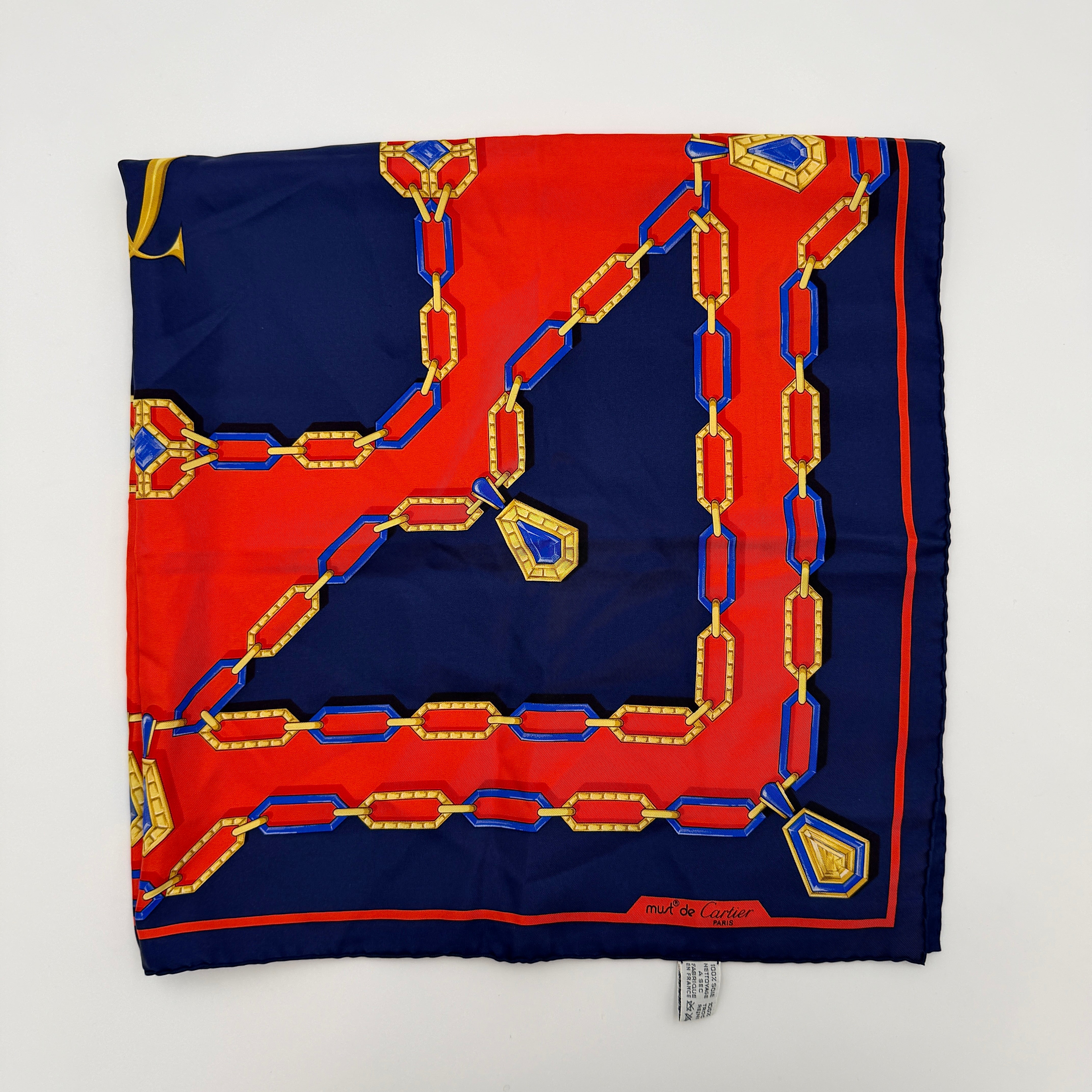 Cartier Must de Cartier silk scarf with striking navy, red, and gold chain motif and jewel accents, styled in a folded drape.