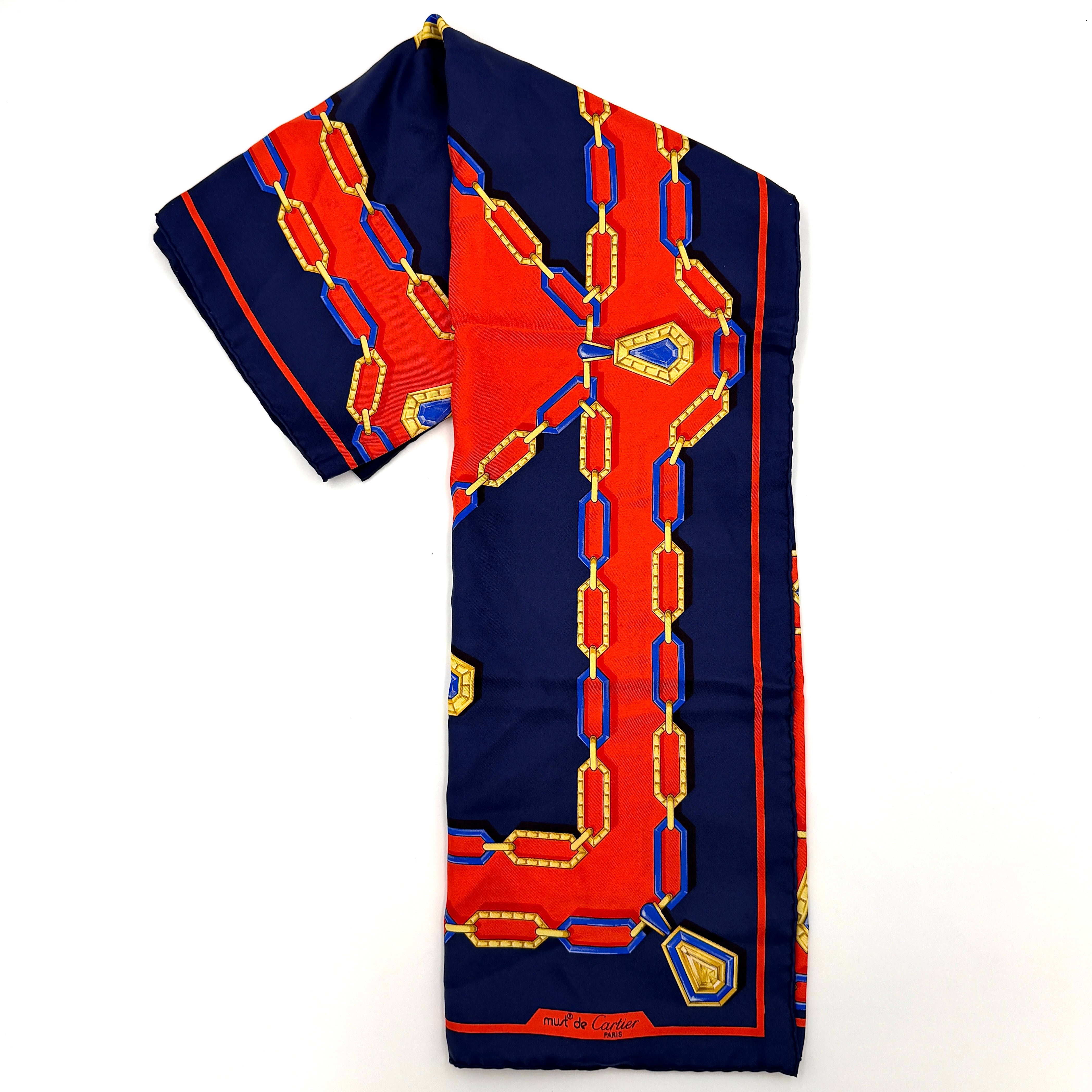Cartier Must de Cartier silk scarf with striking navy, red, and gold chain motif and jewel accents, styled in a folded drape.