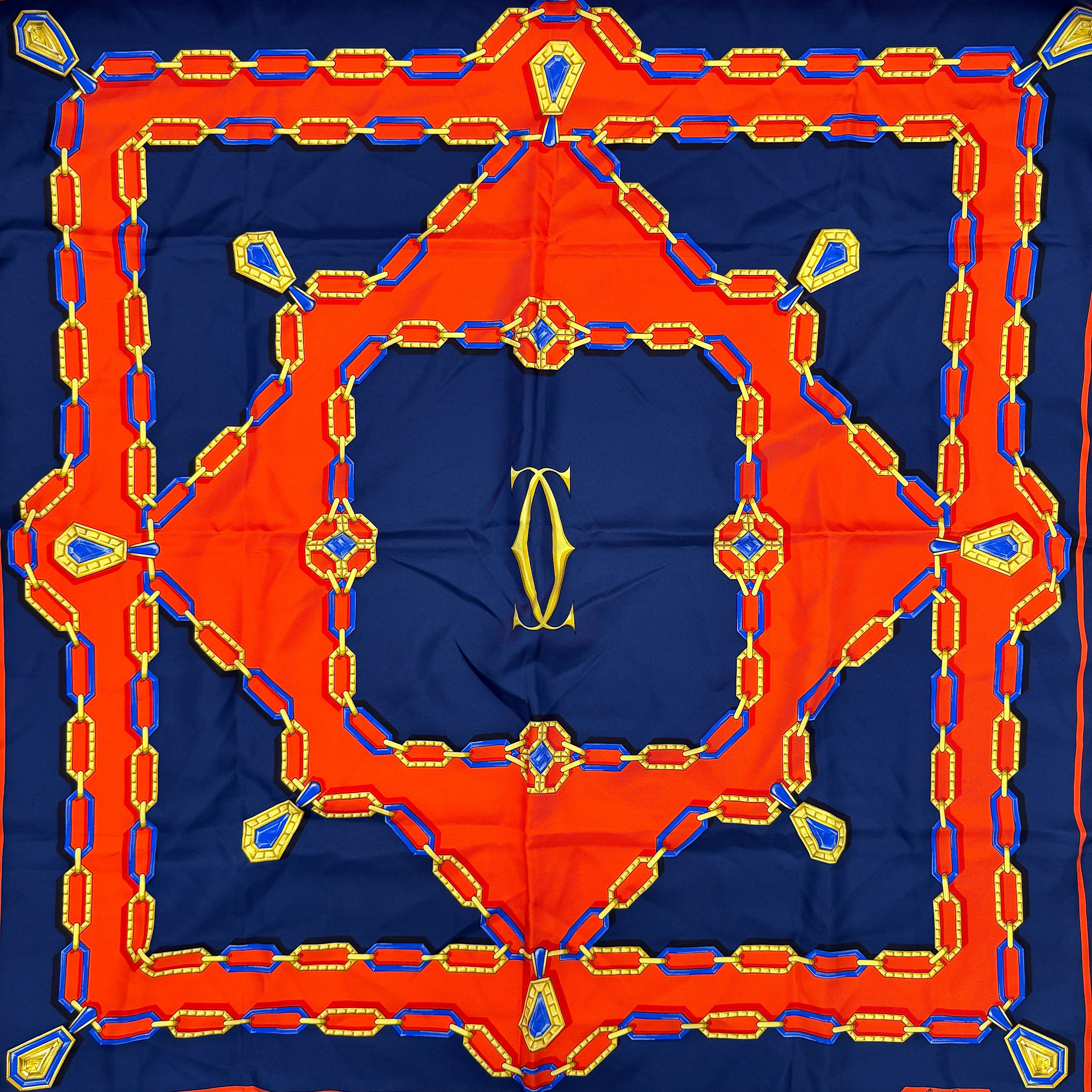 Cartier Must de Cartier silk scarf with striking navy, red, and gold chain motif and jewel accents, styled in a folded drape.