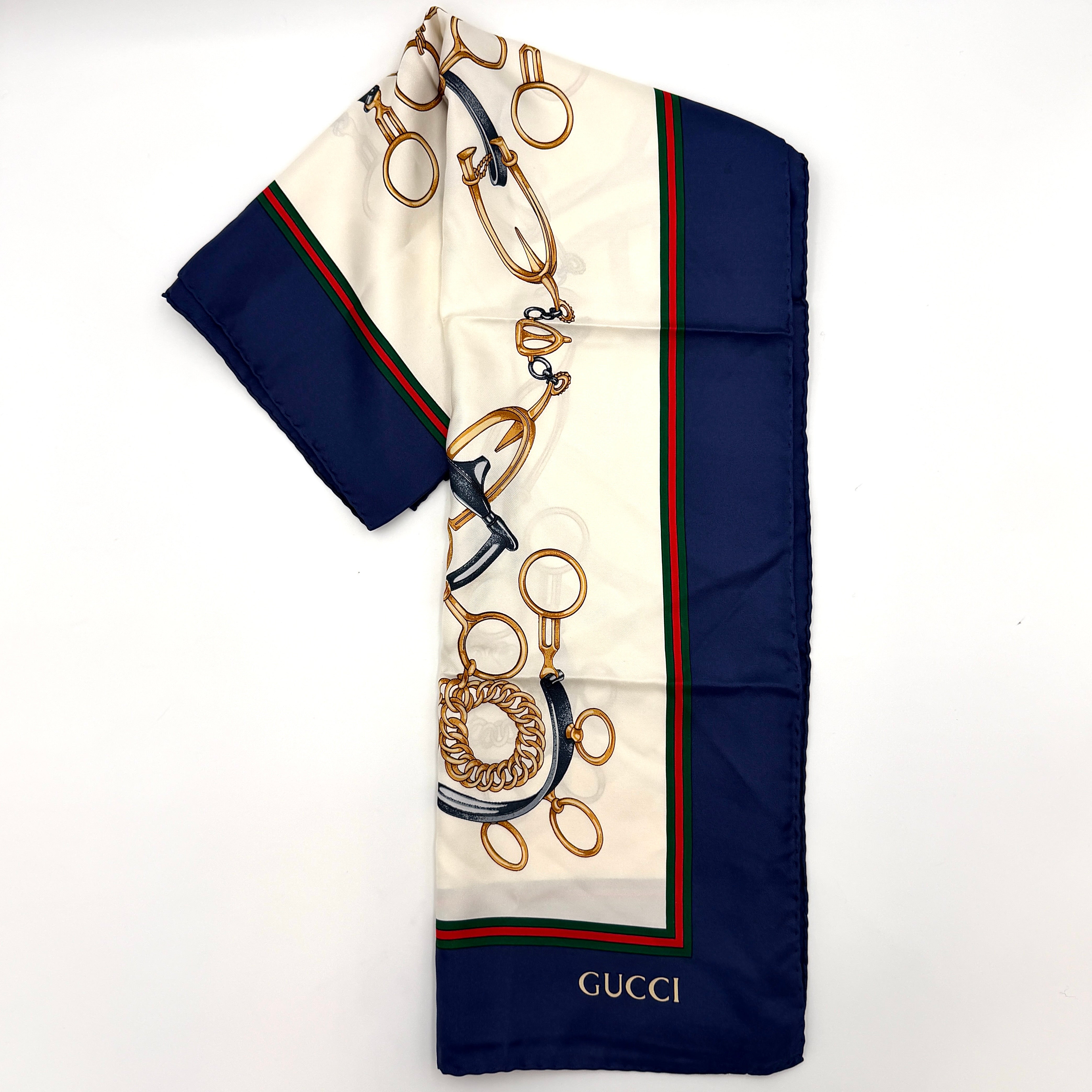 Gucci silk scarf with equestrian horsebit print, navy borders, and large GG logo displayed against a white background.